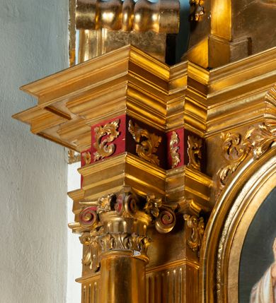 Zdjęcie nr 17: Nastawa architektoniczna, jednoosiowa, dwukondygnacyjna. Ołtarz murowany, prostopadłościenny, obity metalową blachą, zdobioną trybowaną kratownicą i gwiazdkami. Wewnątrz grób Chrystusa ze współczesną rzeźbą. Nastawa na niskim cokole, z wyodrębnionymi dwoma, ukośnie ustawionymi prostopadłościanami, z konsolami, dekorowanymi akantem i kampanulami. Pośrodku cokołu zamontowany obraz św. Faustyny w kształcie wieloboku. Kondygnacja flankowana dwiema parami pilastrów o kanelowanych trzonach oraz ustawioną przed nimi parą kolumn o kapitelach kompozytowych. Podpory dźwigają pełne belkowanie, wyłamane na ich osi, z silnie wysuniętym gzymsem, z przerwanym architrawem i fryzem nad polem środkowym. Na belkowaniu fragmenty przerwanego, wolutowego przyczółka, zwrócone pod kątem, do wewnątrz. W polu środkowym wnęka w formie stojącego prostokąta zamkniętego łukiem półkolistym, ujęta profilowaną ramą dekorowaną na bokach kwiatami, zwieńczoną muszlą. We wnęce obraz „Jezu Ufam Tobie”. Na konsolach, po bokach nastawy ustawione figury św. Kazimierza i św. Jana Kantego. Nastawa flankowana uszami utworzonymi z karbowanej wstęgi i ornamentu roślinnego. Druga kondygnacja węższa, flankowana ustawionymi pod kątem pilastrami, o trzonach dekorowanych kampanulami. Pilastry podtrzymują gzyms wyłamany na ich osi, nad polem przyjmujący kształt łuku półkolistego nadwieszonego. Na nim ustawione dwa wazony z kwiatami i bukiet kwiatów. W polu obraz św. Joachima w formie stojącego owalu, ujęty ramą, dekorowaną ornamentem roślinnym. Struktura niemal w całości złocona, elementy cokołu i fryzu polichromowane w kolorze czerwonym, ornamentyka złocona. 


