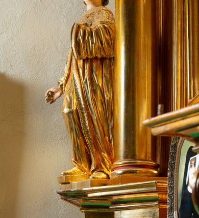 Zdjęcie nr 27: Nastawa architektoniczna, jednoosiowa, dwukondygnacyjna. Ołtarz murowany, prostopadłościenny, obity metalową blachą, zdobioną trybowaną kratownicą i gwiazdkami. Wewnątrz grób Chrystusa ze współczesną rzeźbą. Nastawa na niskim cokole, z wyodrębnionymi dwoma, ukośnie ustawionymi prostopadłościanami, z konsolami, dekorowanymi akantem i kampanulami. Pośrodku cokołu zamontowany obraz św. Faustyny w kształcie wieloboku. Kondygnacja flankowana dwiema parami pilastrów o kanelowanych trzonach oraz ustawioną przed nimi parą kolumn o kapitelach kompozytowych. Podpory dźwigają pełne belkowanie, wyłamane na ich osi, z silnie wysuniętym gzymsem, z przerwanym architrawem i fryzem nad polem środkowym. Na belkowaniu fragmenty przerwanego, wolutowego przyczółka, zwrócone pod kątem, do wewnątrz. W polu środkowym wnęka w formie stojącego prostokąta zamkniętego łukiem półkolistym, ujęta profilowaną ramą dekorowaną na bokach kwiatami, zwieńczoną muszlą. We wnęce obraz „Jezu Ufam Tobie”. Na konsolach, po bokach nastawy ustawione figury św. Kazimierza i św. Jana Kantego. Nastawa flankowana uszami utworzonymi z karbowanej wstęgi i ornamentu roślinnego. Druga kondygnacja węższa, flankowana ustawionymi pod kątem pilastrami, o trzonach dekorowanych kampanulami. Pilastry podtrzymują gzyms wyłamany na ich osi, nad polem przyjmujący kształt łuku półkolistego nadwieszonego. Na nim ustawione dwa wazony z kwiatami i bukiet kwiatów. W polu obraz św. Joachima w formie stojącego owalu, ujęty ramą, dekorowaną ornamentem roślinnym. Struktura niemal w całości złocona, elementy cokołu i fryzu polichromowane w kolorze czerwonym, ornamentyka złocona. 


