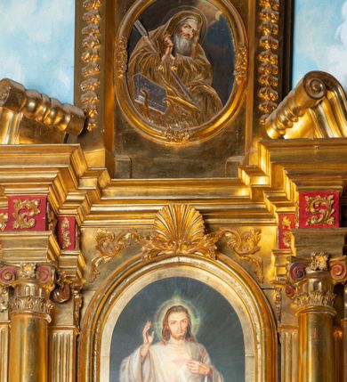 Zdjęcie nr 46: Nastawa architektoniczna, jednoosiowa, dwukondygnacyjna. Ołtarz murowany, prostopadłościenny, obity metalową blachą, zdobioną trybowaną kratownicą i gwiazdkami. Wewnątrz grób Chrystusa ze współczesną rzeźbą. Nastawa na niskim cokole, z wyodrębnionymi dwoma, ukośnie ustawionymi prostopadłościanami, z konsolami, dekorowanymi akantem i kampanulami. Pośrodku cokołu zamontowany obraz św. Faustyny w kształcie wieloboku. Kondygnacja flankowana dwiema parami pilastrów o kanelowanych trzonach oraz ustawioną przed nimi parą kolumn o kapitelach kompozytowych. Podpory dźwigają pełne belkowanie, wyłamane na ich osi, z silnie wysuniętym gzymsem, z przerwanym architrawem i fryzem nad polem środkowym. Na belkowaniu fragmenty przerwanego, wolutowego przyczółka, zwrócone pod kątem, do wewnątrz. W polu środkowym wnęka w formie stojącego prostokąta zamkniętego łukiem półkolistym, ujęta profilowaną ramą dekorowaną na bokach kwiatami, zwieńczoną muszlą. We wnęce obraz „Jezu Ufam Tobie”. Na konsolach, po bokach nastawy ustawione figury św. Kazimierza i św. Jana Kantego. Nastawa flankowana uszami utworzonymi z karbowanej wstęgi i ornamentu roślinnego. Druga kondygnacja węższa, flankowana ustawionymi pod kątem pilastrami, o trzonach dekorowanych kampanulami. Pilastry podtrzymują gzyms wyłamany na ich osi, nad polem przyjmujący kształt łuku półkolistego nadwieszonego. Na nim ustawione dwa wazony z kwiatami i bukiet kwiatów. W polu obraz św. Joachima w formie stojącego owalu, ujęty ramą, dekorowaną ornamentem roślinnym. Struktura niemal w całości złocona, elementy cokołu i fryzu polichromowane w kolorze czerwonym, ornamentyka złocona. 


