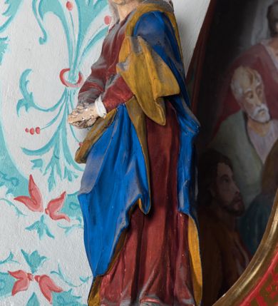 Zdjęcie nr 3: Drewniana belka o wklęsło-wypukłej formie utworzona z dwóch  stykających się wolut. Na jej froncie napis: „JEZU CHRYSTE ZMIŁUJ SIĘ NAD NAMI”. W centrum krzyż z figurą umarłego Chrystusa przybitą trzema gwoździami. Ciało w lekkim zwisie, o szeroko rozłożonych ramionach, z głową opadającą na prawy bark oraz stopami skrzyżowanymi w układzie prawa na lewą. Twarz ma szczupłą, o zamkniętych oczach, garbatym nosie i wąskich ustach, okoloną krótką brodą oraz kręconymi, brązowymi włosami opadającymi na ramiona. Na głowie ma koronę cierniową. Ciało jest wychudzone, o podkreślonych mięśniach ramion i nóg oraz żebrach klatki piersiowej. Przez biodra przewiązane krótkie, ekspresyjnie drapowane perizonium, rozwiane po bokach. Pionowa belka krzyża zwieńczona tabliczką z napisem „INRI”. 
Po lewej stronie krzyża figura Marii, ukazana frontalnie, w kontrapoście, pochylona, z dłońmi splecionymi z przodu. Twarz ma szczupłą, o małych oczach, prostym nosie i wąskich ustach. Ubrana jest w ciemnoczerwoną suknię, przepasaną w talii oraz niebieski płaszcz z jasnobrązową podszewką, zarzucony na lewe ramię i zawinięty wokół postaci. 
Po prawej stronie krzyża figura św. Jana, zwrócona w trzech czwartych w prawo, w kontrapoście, z uniesioną głową oraz rękami skierowanymi w prawo, z prawą w geście wskazującym. Twarz ma szczupłą, o oczach skierowanych w górę, prostym nosie i rozchylonych ustach, okoloną falowanymi włosami opadającymi na ramiona. Ubrany jest w jasnobrązową tunikę, przepasaną w talii oraz niebieski płaszcz z ciemnoczerwoną podszewką, zarzucony na prawe ramię i zawiązany na lewym boku. Polichromia ciał postaci naturalistyczna. 