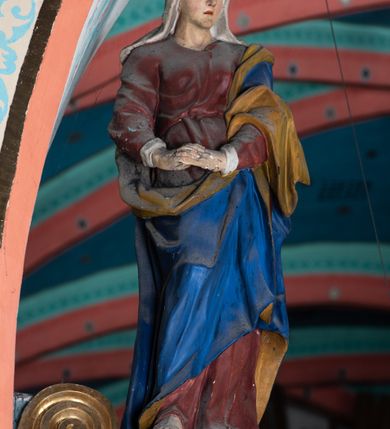 Zdjęcie nr 11: Drewniana belka o wklęsło-wypukłej formie utworzona z dwóch  stykających się wolut. Na jej froncie napis: „JEZU CHRYSTE ZMIŁUJ SIĘ NAD NAMI”. W centrum krzyż z figurą umarłego Chrystusa przybitą trzema gwoździami. Ciało w lekkim zwisie, o szeroko rozłożonych ramionach, z głową opadającą na prawy bark oraz stopami skrzyżowanymi w układzie prawa na lewą. Twarz ma szczupłą, o zamkniętych oczach, garbatym nosie i wąskich ustach, okoloną krótką brodą oraz kręconymi, brązowymi włosami opadającymi na ramiona. Na głowie ma koronę cierniową. Ciało jest wychudzone, o podkreślonych mięśniach ramion i nóg oraz żebrach klatki piersiowej. Przez biodra przewiązane krótkie, ekspresyjnie drapowane perizonium, rozwiane po bokach. Pionowa belka krzyża zwieńczona tabliczką z napisem „INRI”. 
Po lewej stronie krzyża figura Marii, ukazana frontalnie, w kontrapoście, pochylona, z dłońmi splecionymi z przodu. Twarz ma szczupłą, o małych oczach, prostym nosie i wąskich ustach. Ubrana jest w ciemnoczerwoną suknię, przepasaną w talii oraz niebieski płaszcz z jasnobrązową podszewką, zarzucony na lewe ramię i zawinięty wokół postaci. 
Po prawej stronie krzyża figura św. Jana, zwrócona w trzech czwartych w prawo, w kontrapoście, z uniesioną głową oraz rękami skierowanymi w prawo, z prawą w geście wskazującym. Twarz ma szczupłą, o oczach skierowanych w górę, prostym nosie i rozchylonych ustach, okoloną falowanymi włosami opadającymi na ramiona. Ubrany jest w jasnobrązową tunikę, przepasaną w talii oraz niebieski płaszcz z ciemnoczerwoną podszewką, zarzucony na prawe ramię i zawiązany na lewym boku. Polichromia ciał postaci naturalistyczna. 