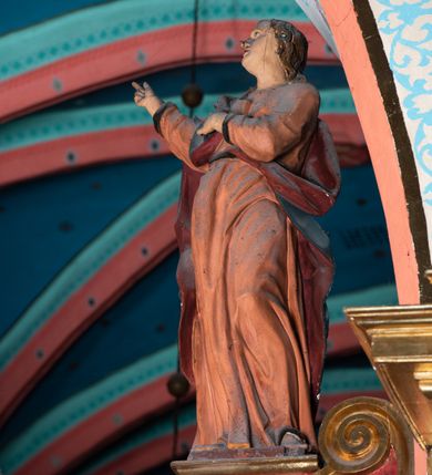 Zdjęcie nr 7: Drewniana belka o wklęsło-wypukłej formie utworzona z dwóch  stykających się wolut. Na jej froncie napis: „JEZU CHRYSTE ZMIŁUJ SIĘ NAD NAMI”. W centrum krzyż z figurą umarłego Chrystusa przybitą trzema gwoździami. Ciało w lekkim zwisie, o szeroko rozłożonych ramionach, z głową opadającą na prawy bark oraz stopami skrzyżowanymi w układzie prawa na lewą. Twarz ma szczupłą, o zamkniętych oczach, garbatym nosie i wąskich ustach, okoloną krótką brodą oraz kręconymi, brązowymi włosami opadającymi na ramiona. Na głowie ma koronę cierniową. Ciało jest wychudzone, o podkreślonych mięśniach ramion i nóg oraz żebrach klatki piersiowej. Przez biodra przewiązane krótkie, ekspresyjnie drapowane perizonium, rozwiane po bokach. Pionowa belka krzyża zwieńczona tabliczką z napisem „INRI”. 
Po lewej stronie krzyża figura Marii, ukazana frontalnie, w kontrapoście, pochylona, z dłońmi splecionymi z przodu. Twarz ma szczupłą, o małych oczach, prostym nosie i wąskich ustach. Ubrana jest w ciemnoczerwoną suknię, przepasaną w talii oraz niebieski płaszcz z jasnobrązową podszewką, zarzucony na lewe ramię i zawinięty wokół postaci. 
Po prawej stronie krzyża figura św. Jana, zwrócona w trzech czwartych w prawo, w kontrapoście, z uniesioną głową oraz rękami skierowanymi w prawo, z prawą w geście wskazującym. Twarz ma szczupłą, o oczach skierowanych w górę, prostym nosie i rozchylonych ustach, okoloną falowanymi włosami opadającymi na ramiona. Ubrany jest w jasnobrązową tunikę, przepasaną w talii oraz niebieski płaszcz z ciemnoczerwoną podszewką, zarzucony na prawe ramię i zawiązany na lewym boku. Polichromia ciał postaci naturalistyczna. 