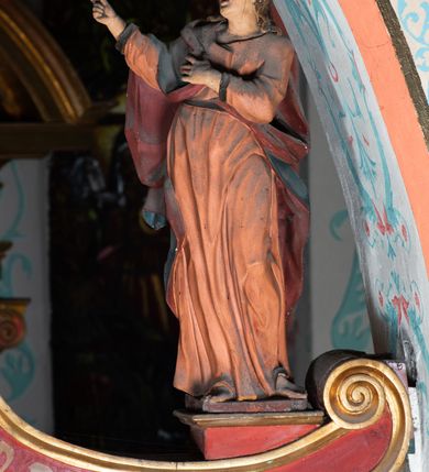 Zdjęcie nr 9: Drewniana belka o wklęsło-wypukłej formie utworzona z dwóch  stykających się wolut. Na jej froncie napis: „JEZU CHRYSTE ZMIŁUJ SIĘ NAD NAMI”. W centrum krzyż z figurą umarłego Chrystusa przybitą trzema gwoździami. Ciało w lekkim zwisie, o szeroko rozłożonych ramionach, z głową opadającą na prawy bark oraz stopami skrzyżowanymi w układzie prawa na lewą. Twarz ma szczupłą, o zamkniętych oczach, garbatym nosie i wąskich ustach, okoloną krótką brodą oraz kręconymi, brązowymi włosami opadającymi na ramiona. Na głowie ma koronę cierniową. Ciało jest wychudzone, o podkreślonych mięśniach ramion i nóg oraz żebrach klatki piersiowej. Przez biodra przewiązane krótkie, ekspresyjnie drapowane perizonium, rozwiane po bokach. Pionowa belka krzyża zwieńczona tabliczką z napisem „INRI”. 
Po lewej stronie krzyża figura Marii, ukazana frontalnie, w kontrapoście, pochylona, z dłońmi splecionymi z przodu. Twarz ma szczupłą, o małych oczach, prostym nosie i wąskich ustach. Ubrana jest w ciemnoczerwoną suknię, przepasaną w talii oraz niebieski płaszcz z jasnobrązową podszewką, zarzucony na lewe ramię i zawinięty wokół postaci. 
Po prawej stronie krzyża figura św. Jana, zwrócona w trzech czwartych w prawo, w kontrapoście, z uniesioną głową oraz rękami skierowanymi w prawo, z prawą w geście wskazującym. Twarz ma szczupłą, o oczach skierowanych w górę, prostym nosie i rozchylonych ustach, okoloną falowanymi włosami opadającymi na ramiona. Ubrany jest w jasnobrązową tunikę, przepasaną w talii oraz niebieski płaszcz z ciemnoczerwoną podszewką, zarzucony na prawe ramię i zawiązany na lewym boku. Polichromia ciał postaci naturalistyczna. 