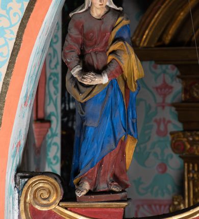 Zdjęcie nr 10: Drewniana belka o wklęsło-wypukłej formie utworzona z dwóch  stykających się wolut. Na jej froncie napis: „JEZU CHRYSTE ZMIŁUJ SIĘ NAD NAMI”. W centrum krzyż z figurą umarłego Chrystusa przybitą trzema gwoździami. Ciało w lekkim zwisie, o szeroko rozłożonych ramionach, z głową opadającą na prawy bark oraz stopami skrzyżowanymi w układzie prawa na lewą. Twarz ma szczupłą, o zamkniętych oczach, garbatym nosie i wąskich ustach, okoloną krótką brodą oraz kręconymi, brązowymi włosami opadającymi na ramiona. Na głowie ma koronę cierniową. Ciało jest wychudzone, o podkreślonych mięśniach ramion i nóg oraz żebrach klatki piersiowej. Przez biodra przewiązane krótkie, ekspresyjnie drapowane perizonium, rozwiane po bokach. Pionowa belka krzyża zwieńczona tabliczką z napisem „INRI”. 
Po lewej stronie krzyża figura Marii, ukazana frontalnie, w kontrapoście, pochylona, z dłońmi splecionymi z przodu. Twarz ma szczupłą, o małych oczach, prostym nosie i wąskich ustach. Ubrana jest w ciemnoczerwoną suknię, przepasaną w talii oraz niebieski płaszcz z jasnobrązową podszewką, zarzucony na lewe ramię i zawinięty wokół postaci. 
Po prawej stronie krzyża figura św. Jana, zwrócona w trzech czwartych w prawo, w kontrapoście, z uniesioną głową oraz rękami skierowanymi w prawo, z prawą w geście wskazującym. Twarz ma szczupłą, o oczach skierowanych w górę, prostym nosie i rozchylonych ustach, okoloną falowanymi włosami opadającymi na ramiona. Ubrany jest w jasnobrązową tunikę, przepasaną w talii oraz niebieski płaszcz z ciemnoczerwoną podszewką, zarzucony na prawe ramię i zawiązany na lewym boku. Polichromia ciał postaci naturalistyczna. 