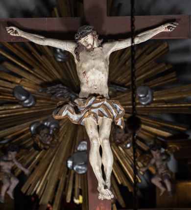 Zdjęcie nr 1: Drewniana belka o wklęsło-wypukłej formie utworzona z dwóch  stykających się wolut. Na jej froncie napis: „JEZU CHRYSTE ZMIŁUJ SIĘ NAD NAMI”. W centrum krzyż z figurą umarłego Chrystusa przybitą trzema gwoździami. Ciało w lekkim zwisie, o szeroko rozłożonych ramionach, z głową opadającą na prawy bark oraz stopami skrzyżowanymi w układzie prawa na lewą. Twarz ma szczupłą, o zamkniętych oczach, garbatym nosie i wąskich ustach, okoloną krótką brodą oraz kręconymi, brązowymi włosami opadającymi na ramiona. Na głowie ma koronę cierniową. Ciało jest wychudzone, o podkreślonych mięśniach ramion i nóg oraz żebrach klatki piersiowej. Przez biodra przewiązane krótkie, ekspresyjnie drapowane perizonium, rozwiane po bokach. Pionowa belka krzyża zwieńczona tabliczką z napisem „INRI”. 
Po lewej stronie krzyża figura Marii, ukazana frontalnie, w kontrapoście, pochylona, z dłońmi splecionymi z przodu. Twarz ma szczupłą, o małych oczach, prostym nosie i wąskich ustach. Ubrana jest w ciemnoczerwoną suknię, przepasaną w talii oraz niebieski płaszcz z jasnobrązową podszewką, zarzucony na lewe ramię i zawinięty wokół postaci. 
Po prawej stronie krzyża figura św. Jana, zwrócona w trzech czwartych w prawo, w kontrapoście, z uniesioną głową oraz rękami skierowanymi w prawo, z prawą w geście wskazującym. Twarz ma szczupłą, o oczach skierowanych w górę, prostym nosie i rozchylonych ustach, okoloną falowanymi włosami opadającymi na ramiona. Ubrany jest w jasnobrązową tunikę, przepasaną w talii oraz niebieski płaszcz z ciemnoczerwoną podszewką, zarzucony na prawe ramię i zawiązany na lewym boku. Polichromia ciał postaci naturalistyczna. 