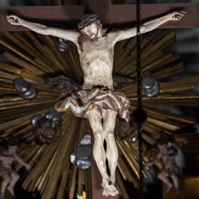Zdjęcie nr 1: Drewniana belka o wklęsło-wypukłej formie utworzona z dwóch  stykających się wolut. Na jej froncie napis: „JEZU CHRYSTE ZMIŁUJ SIĘ NAD NAMI”. W centrum krzyż z figurą umarłego Chrystusa przybitą trzema gwoździami. Ciało w lekkim zwisie, o szeroko rozłożonych ramionach, z głową opadającą na prawy bark oraz stopami skrzyżowanymi w układzie prawa na lewą. Twarz ma szczupłą, o zamkniętych oczach, garbatym nosie i wąskich ustach, okoloną krótką brodą oraz kręconymi, brązowymi włosami opadającymi na ramiona. Na głowie ma koronę cierniową. Ciało jest wychudzone, o podkreślonych mięśniach ramion i nóg oraz żebrach klatki piersiowej. Przez biodra przewiązane krótkie, ekspresyjnie drapowane perizonium, rozwiane po bokach. Pionowa belka krzyża zwieńczona tabliczką z napisem „INRI”. 
Po lewej stronie krzyża figura Marii, ukazana frontalnie, w kontrapoście, pochylona, z dłońmi splecionymi z przodu. Twarz ma szczupłą, o małych oczach, prostym nosie i wąskich ustach. Ubrana jest w ciemnoczerwoną suknię, przepasaną w talii oraz niebieski płaszcz z jasnobrązową podszewką, zarzucony na lewe ramię i zawinięty wokół postaci. 
Po prawej stronie krzyża figura św. Jana, zwrócona w trzech czwartych w prawo, w kontrapoście, z uniesioną głową oraz rękami skierowanymi w prawo, z prawą w geście wskazującym. Twarz ma szczupłą, o oczach skierowanych w górę, prostym nosie i rozchylonych ustach, okoloną falowanymi włosami opadającymi na ramiona. Ubrany jest w jasnobrązową tunikę, przepasaną w talii oraz niebieski płaszcz z ciemnoczerwoną podszewką, zarzucony na prawe ramię i zawiązany na lewym boku. Polichromia ciał postaci naturalistyczna. 