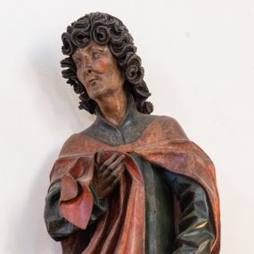 Zdjęcie nr 1: Pełnoplastyczna rzeźba ustawiona na niewielkiej, owalnej podstawie. Święty Jan przedstawiony całopostaciowo, w pozycji stojącej z ciałem zwróconym w trzech czwartych w prawo. Został ukazany jako szczupły mężczyzna o bujnych, kręconych włosach w kolorze ciemnobrązowym tworzących głęboko rzeźbione loki oraz chudej, „kościstej” twarzy z wyraźnie zaznaczonymi łukami brwiowymi i kośćmi policzkowymi. Wzrok uniesiony ku górze. Postać w lewej ręce trzyma księgę umieszczoną w brązowej sakiewce, prawą podtrzymuje połę płaszcza. Święty ubrany jest w ciemnozieloną, sięgającą ziemi szatę z długimi rękawami i wysokim kołnierzem oraz czerwony płaszcz. Spod szat widoczne są bose stopy. Figura w pełni polichromowana.