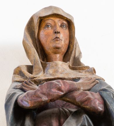 Zdjęcie nr 1: Rzeźba pełna, ustawiona na niewielkiej, owalnej podstawie. Maria przedstawiona frontalnie, w pozycji stojącej z rękami skrzyżowanymi na wysokości piersi. Matka Chrystusa została przedstawiona jako szczupła kobieta o owalnej twarzy o zasmuconym wyrazie. Wyraźnie zaznaczone łuki brwiowe, długi prosty nos i niewielkie usta. Oczy skierowane przed siebie. Dłonie o długich i szczupłych palcach. Maria ubrana jest w fioletową suknię z długimi rękawami oraz obszerny, ciemnogranatowy płaszcz szczelnie otulający ciało i tworzący głęboko łamane, ostre fałdy. Na głowie Marii biała chusta oraz podwika. Figura w pełni polichromowana.