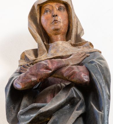 Zdjęcie nr 2: Rzeźba pełna, ustawiona na niewielkiej, owalnej podstawie. Maria przedstawiona frontalnie, w pozycji stojącej z rękami skrzyżowanymi na wysokości piersi. Matka Chrystusa została przedstawiona jako szczupła kobieta o owalnej twarzy o zasmuconym wyrazie. Wyraźnie zaznaczone łuki brwiowe, długi prosty nos i niewielkie usta. Oczy skierowane przed siebie. Dłonie o długich i szczupłych palcach. Maria ubrana jest w fioletową suknię z długimi rękawami oraz obszerny, ciemnogranatowy płaszcz szczelnie otulający ciało i tworzący głęboko łamane, ostre fałdy. Na głowie Marii biała chusta oraz podwika. Figura w pełni polichromowana.