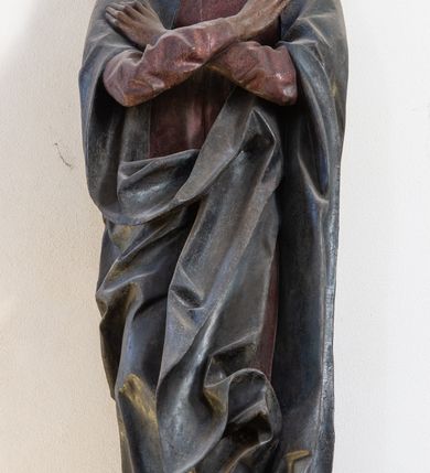 Zdjęcie nr 4: Rzeźba pełna, ustawiona na niewielkiej, owalnej podstawie. Maria przedstawiona frontalnie, w pozycji stojącej z rękami skrzyżowanymi na wysokości piersi. Matka Chrystusa została przedstawiona jako szczupła kobieta o owalnej twarzy o zasmuconym wyrazie. Wyraźnie zaznaczone łuki brwiowe, długi prosty nos i niewielkie usta. Oczy skierowane przed siebie. Dłonie o długich i szczupłych palcach. Maria ubrana jest w fioletową suknię z długimi rękawami oraz obszerny, ciemnogranatowy płaszcz szczelnie otulający ciało i tworzący głęboko łamane, ostre fałdy. Na głowie Marii biała chusta oraz podwika. Figura w pełni polichromowana.