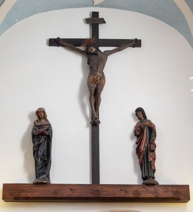 Zdjęcie nr 6: Rzeźba pełna, ustawiona na niewielkiej, owalnej podstawie. Maria przedstawiona frontalnie, w pozycji stojącej z rękami skrzyżowanymi na wysokości piersi. Matka Chrystusa została przedstawiona jako szczupła kobieta o owalnej twarzy o zasmuconym wyrazie. Wyraźnie zaznaczone łuki brwiowe, długi prosty nos i niewielkie usta. Oczy skierowane przed siebie. Dłonie o długich i szczupłych palcach. Maria ubrana jest w fioletową suknię z długimi rękawami oraz obszerny, ciemnogranatowy płaszcz szczelnie otulający ciało i tworzący głęboko łamane, ostre fałdy. Na głowie Marii biała chusta oraz podwika. Figura w pełni polichromowana.