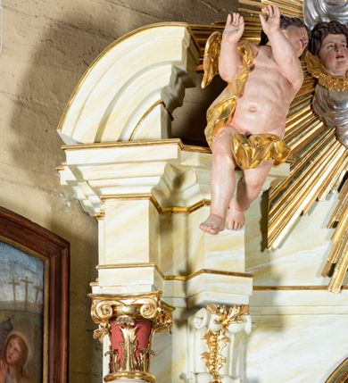 Zdjęcie nr 12: Ołtarz architektoniczny, jednokondygnacyjny, jednoosiowy ze zwieńczeniem i drewnianą, sarkofagową mensą. Na mensie ołtarza kremowe tabernakulum w formie prostopadłościennej szafki, ujęte parą jońskich, złoconych półkolumienek, stojących na profilowanym  cokoliku, wspierających belkowanie przechodzące nad polem centralnym w łuk. Drzwiczki w kształcie stojącego prostokąta zamkniętego łukiem pełnym zdobione płaskorzeźbionym motywem kielicha z hostią w glorii. Retabulum ołtarzowe na cokole, ujęte parą kolumn kompozytowych o spiralnie skręconych trzonach.  Podpory wspierają wyłamujące się ponad nimi oraz między nimi belkowanie o wysuniętym gzymsie, podtrzymujące przerwane fragmenty przyczółka. Pole środkowe w formie wnęki w kształcie stojącego prostokąta zamkniętego łukiem nadwieszonym z obrazem św. Anny Samotrzeć. Ujmuje ją para figur ustawionych na wysokich, zdwojonych cokołach. Postać z lewej strony trzyma berło, postać z prawej jabłko królewskie.  Zwieńczenie w formie stojącego owalu ujętego skłębionymi obłokami i szeroką glorią promienistą. W polu przedstawienie Matki Boskiej ujęte główkami anielskimi i parą putt. 
 Pola cokołu dekorowane płycinami. Na trzonach kolumn retabulum spiralnie oplatająca je wić roślinna. Wewnętrzne fragmenty wyłamanego gzymsu podtrzymują konsole, pod którymi podwieszono bukiety kwiatów. Struktura ołtarza polichromowana z imitacją marmoryzacji w odcieniach białym i kremowym, tło głowic kolumn czerwone, dekoracje i profile złocone i srebrzone. 
