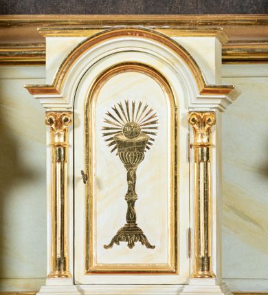 Zdjęcie nr 16: Ołtarz architektoniczny, jednokondygnacyjny, jednoosiowy ze zwieńczeniem i drewnianą, sarkofagową mensą. Na mensie ołtarza kremowe tabernakulum w formie prostopadłościennej szafki, ujęte parą jońskich, złoconych półkolumienek, stojących na profilowanym  cokoliku, wspierających belkowanie przechodzące nad polem centralnym w łuk. Drzwiczki w kształcie stojącego prostokąta zamkniętego łukiem pełnym zdobione płaskorzeźbionym motywem kielicha z hostią w glorii. Retabulum ołtarzowe na cokole, ujęte parą kolumn kompozytowych o spiralnie skręconych trzonach.  Podpory wspierają wyłamujące się ponad nimi oraz między nimi belkowanie o wysuniętym gzymsie, podtrzymujące przerwane fragmenty przyczółka. Pole środkowe w formie wnęki w kształcie stojącego prostokąta zamkniętego łukiem nadwieszonym z obrazem św. Anny Samotrzeć. Ujmuje ją para figur ustawionych na wysokich, zdwojonych cokołach. Postać z lewej strony trzyma berło, postać z prawej jabłko królewskie.  Zwieńczenie w formie stojącego owalu ujętego skłębionymi obłokami i szeroką glorią promienistą. W polu przedstawienie Matki Boskiej ujęte główkami anielskimi i parą putt. 
 Pola cokołu dekorowane płycinami. Na trzonach kolumn retabulum spiralnie oplatająca je wić roślinna. Wewnętrzne fragmenty wyłamanego gzymsu podtrzymują konsole, pod którymi podwieszono bukiety kwiatów. Struktura ołtarza polichromowana z imitacją marmoryzacji w odcieniach białym i kremowym, tło głowic kolumn czerwone, dekoracje i profile złocone i srebrzone. 
