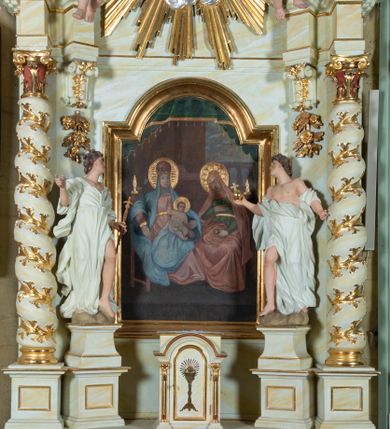 Zdjęcie nr 1: Ołtarz architektoniczny, jednokondygnacyjny, jednoosiowy ze zwieńczeniem i drewnianą, sarkofagową mensą. Na mensie ołtarza kremowe tabernakulum w formie prostopadłościennej szafki, ujęte parą jońskich, złoconych półkolumienek, stojących na profilowanym  cokoliku, wspierających belkowanie przechodzące nad polem centralnym w łuk. Drzwiczki w kształcie stojącego prostokąta zamkniętego łukiem pełnym zdobione płaskorzeźbionym motywem kielicha z hostią w glorii. Retabulum ołtarzowe na cokole, ujęte parą kolumn kompozytowych o spiralnie skręconych trzonach.  Podpory wspierają wyłamujące się ponad nimi oraz między nimi belkowanie o wysuniętym gzymsie, podtrzymujące przerwane fragmenty przyczółka. Pole środkowe w formie wnęki w kształcie stojącego prostokąta zamkniętego łukiem nadwieszonym z obrazem św. Anny Samotrzeć. Ujmuje ją para figur ustawionych na wysokich, zdwojonych cokołach. Postać z lewej strony trzyma berło, postać z prawej jabłko królewskie.  Zwieńczenie w formie stojącego owalu ujętego skłębionymi obłokami i szeroką glorią promienistą. W polu przedstawienie Matki Boskiej ujęte główkami anielskimi i parą putt. 
 Pola cokołu dekorowane płycinami. Na trzonach kolumn retabulum spiralnie oplatająca je wić roślinna. Wewnętrzne fragmenty wyłamanego gzymsu podtrzymują konsole, pod którymi podwieszono bukiety kwiatów. Struktura ołtarza polichromowana z imitacją marmoryzacji w odcieniach białym i kremowym, tło głowic kolumn czerwone, dekoracje i profile złocone i srebrzone. 
