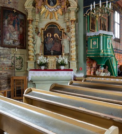 Zdjęcie nr 2: Ołtarz architektoniczny, jednokondygnacyjny, jednoosiowy ze zwieńczeniem i drewnianą, sarkofagową mensą. Na mensie ołtarza kremowe tabernakulum w formie prostopadłościennej szafki, ujęte parą jońskich, złoconych półkolumienek, stojących na profilowanym  cokoliku, wspierających belkowanie przechodzące nad polem centralnym w łuk. Drzwiczki w kształcie stojącego prostokąta zamkniętego łukiem pełnym zdobione płaskorzeźbionym motywem kielicha z hostią w glorii. Retabulum ołtarzowe na cokole, ujęte parą kolumn kompozytowych o spiralnie skręconych trzonach.  Podpory wspierają wyłamujące się ponad nimi oraz między nimi belkowanie o wysuniętym gzymsie, podtrzymujące przerwane fragmenty przyczółka. Pole środkowe w formie wnęki w kształcie stojącego prostokąta zamkniętego łukiem nadwieszonym z obrazem św. Anny Samotrzeć. Ujmuje ją para figur ustawionych na wysokich, zdwojonych cokołach. Postać z lewej strony trzyma berło, postać z prawej jabłko królewskie.  Zwieńczenie w formie stojącego owalu ujętego skłębionymi obłokami i szeroką glorią promienistą. W polu przedstawienie Matki Boskiej ujęte główkami anielskimi i parą putt. 
 Pola cokołu dekorowane płycinami. Na trzonach kolumn retabulum spiralnie oplatająca je wić roślinna. Wewnętrzne fragmenty wyłamanego gzymsu podtrzymują konsole, pod którymi podwieszono bukiety kwiatów. Struktura ołtarza polichromowana z imitacją marmoryzacji w odcieniach białym i kremowym, tło głowic kolumn czerwone, dekoracje i profile złocone i srebrzone. 
