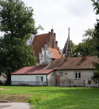 Zdjęcie nr 56: Kościół orientowany, murowany z cegły i kamienia, jednonawowy z trójprzęsłowym prezbiterium zamkniętym wielobocznie, sklepionym krzyżowo-żebrowo. Od północy umieszczona prostokątna, piętrowa zakrystia sklepiona kolebkowo (pięterko nad zakrystią dodane w 1885), dostępna kamiennym portalem o wykroju prostokątnym od strony wschodniej. Ściana północna zakrystii zakończona schodkowo z dekoracją blendową. Również od północy, na szerokości nawy do kościoła przylega prostokątna kaplica nakryta dachem czterospadowym zwieńczonym czworoboczną wieżyczką dostępna od zachodu przez prostokątną kruchtę z portalem o wykroju prostokątnym ujętym dwulalkowymi, kamiennymi balaskami. Kruchta zwieńczona trójkątnym przyczółkiem, na którym kamienny krzyż. Trójprzęsłowa nawa wyższa i szersza od prezbiterium i przesunięta w stosunku do jego osi ku stronie północnej, nakryta stropem. Północny mur nawy w części zachodniej poszerzony do pewnej wysokości dla pomieszczenia w jego grubości schodów prowadzących na chór muzyczny. Okna prostokątne zamknięte łukiem półkolistym. Zachodni i wschodni szczyt nawy zamknięty schodkowo. Od strony wschodniej trzy ostrołukowe blendy, w środkowej, wyżej od bocznych umieszczona tarcza herbowa z wizerunkiem św. Stanisława oraz Orła Białego. Od południa do nawy przylega prostokątna kruchta z kamiennym, ostrołukowym portalem nakryta dachem pulpitowym. Od strony zachodniej do bryły kościoła dostawiona prostokątna, współczesna kruchta wraz z chórem muzycznym (dobudowana w 1966) dostępna portalem o wykroju prostokątnym, nakryta dwuspadowym dachem. W ścianach bocznych wąskie, smukłe okna w kształcie stojącego prostokąta. Ponad kruchtą ażurowa dzwonnica na rzucie trójkąta zwieńczona krzyżem. Wieżyczka na sygnaturkę na rzucie ośmioboku zwieńczona barokowym hełmem z glorietą i krzyżem. Od zewnątrz kościół częściowo tynkowany, nawa i prezbiterium opięte szkarpami. Dachy kryte dachówką oraz blachą (część wschodnia prezbiterium).