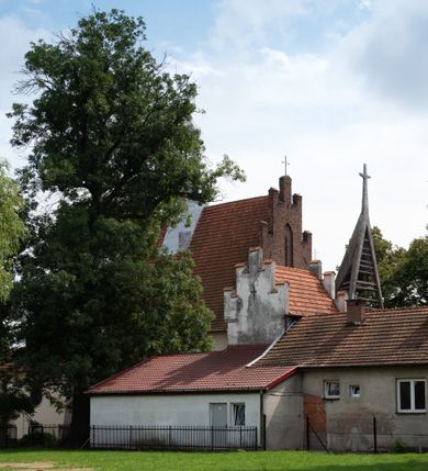 Zdjęcie nr 3: Kościół orientowany, murowany z cegły i kamienia, jednonawowy z trójprzęsłowym prezbiterium zamkniętym wielobocznie, sklepionym krzyżowo-żebrowo. Od północy umieszczona prostokątna, piętrowa zakrystia sklepiona kolebkowo (pięterko nad zakrystią dodane w 1885), dostępna kamiennym portalem o wykroju prostokątnym od strony wschodniej. Ściana północna zakrystii zakończona schodkowo z dekoracją blendową. Również od północy, na szerokości nawy do kościoła przylega prostokątna kaplica nakryta dachem czterospadowym zwieńczonym czworoboczną wieżyczką dostępna od zachodu przez prostokątną kruchtę z portalem o wykroju prostokątnym ujętym dwulalkowymi, kamiennymi balaskami. Kruchta zwieńczona trójkątnym przyczółkiem, na którym kamienny krzyż. Trójprzęsłowa nawa wyższa i szersza od prezbiterium i przesunięta w stosunku do jego osi ku stronie północnej, nakryta stropem. Północny mur nawy w części zachodniej poszerzony do pewnej wysokości dla pomieszczenia w jego grubości schodów prowadzących na chór muzyczny. Okna prostokątne zamknięte łukiem półkolistym. Zachodni i wschodni szczyt nawy zamknięty schodkowo. Od strony wschodniej trzy ostrołukowe blendy, w środkowej, wyżej od bocznych umieszczona tarcza herbowa z wizerunkiem św. Stanisława oraz Orła Białego. Od południa do nawy przylega prostokątna kruchta z kamiennym, ostrołukowym portalem nakryta dachem pulpitowym. Od strony zachodniej do bryły kościoła dostawiona prostokątna, współczesna kruchta wraz z chórem muzycznym (dobudowana w 1966) dostępna portalem o wykroju prostokątnym, nakryta dwuspadowym dachem. W ścianach bocznych wąskie, smukłe okna w kształcie stojącego prostokąta. Ponad kruchtą ażurowa dzwonnica na rzucie trójkąta zwieńczona krzyżem. Wieżyczka na sygnaturkę na rzucie ośmioboku zwieńczona barokowym hełmem z glorietą i krzyżem. Od zewnątrz kościół częściowo tynkowany, nawa i prezbiterium opięte szkarpami. Dachy kryte dachówką oraz blachą (część wschodnia prezbiterium).