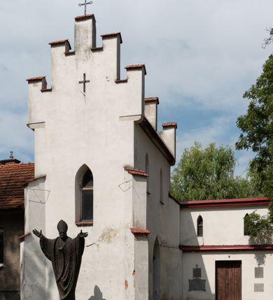 Zdjęcie nr 57: Kościół orientowany, murowany z cegły i kamienia, jednonawowy z trójprzęsłowym prezbiterium zamkniętym wielobocznie, sklepionym krzyżowo-żebrowo. Od północy umieszczona prostokątna, piętrowa zakrystia sklepiona kolebkowo (pięterko nad zakrystią dodane w 1885), dostępna kamiennym portalem o wykroju prostokątnym od strony wschodniej. Ściana północna zakrystii zakończona schodkowo z dekoracją blendową. Również od północy, na szerokości nawy do kościoła przylega prostokątna kaplica nakryta dachem czterospadowym zwieńczonym czworoboczną wieżyczką dostępna od zachodu przez prostokątną kruchtę z portalem o wykroju prostokątnym ujętym dwulalkowymi, kamiennymi balaskami. Kruchta zwieńczona trójkątnym przyczółkiem, na którym kamienny krzyż. Trójprzęsłowa nawa wyższa i szersza od prezbiterium i przesunięta w stosunku do jego osi ku stronie północnej, nakryta stropem. Północny mur nawy w części zachodniej poszerzony do pewnej wysokości dla pomieszczenia w jego grubości schodów prowadzących na chór muzyczny. Okna prostokątne zamknięte łukiem półkolistym. Zachodni i wschodni szczyt nawy zamknięty schodkowo. Od strony wschodniej trzy ostrołukowe blendy, w środkowej, wyżej od bocznych umieszczona tarcza herbowa z wizerunkiem św. Stanisława oraz Orła Białego. Od południa do nawy przylega prostokątna kruchta z kamiennym, ostrołukowym portalem nakryta dachem pulpitowym. Od strony zachodniej do bryły kościoła dostawiona prostokątna, współczesna kruchta wraz z chórem muzycznym (dobudowana w 1966) dostępna portalem o wykroju prostokątnym, nakryta dwuspadowym dachem. W ścianach bocznych wąskie, smukłe okna w kształcie stojącego prostokąta. Ponad kruchtą ażurowa dzwonnica na rzucie trójkąta zwieńczona krzyżem. Wieżyczka na sygnaturkę na rzucie ośmioboku zwieńczona barokowym hełmem z glorietą i krzyżem. Od zewnątrz kościół częściowo tynkowany, nawa i prezbiterium opięte szkarpami. Dachy kryte dachówką oraz blachą (część wschodnia prezbiterium).