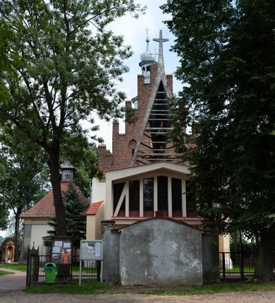 Zdjęcie nr 4: Kościół orientowany, murowany z cegły i kamienia, jednonawowy z trójprzęsłowym prezbiterium zamkniętym wielobocznie, sklepionym krzyżowo-żebrowo. Od północy umieszczona prostokątna, piętrowa zakrystia sklepiona kolebkowo (pięterko nad zakrystią dodane w 1885), dostępna kamiennym portalem o wykroju prostokątnym od strony wschodniej. Ściana północna zakrystii zakończona schodkowo z dekoracją blendową. Również od północy, na szerokości nawy do kościoła przylega prostokątna kaplica nakryta dachem czterospadowym zwieńczonym czworoboczną wieżyczką dostępna od zachodu przez prostokątną kruchtę z portalem o wykroju prostokątnym ujętym dwulalkowymi, kamiennymi balaskami. Kruchta zwieńczona trójkątnym przyczółkiem, na którym kamienny krzyż. Trójprzęsłowa nawa wyższa i szersza od prezbiterium i przesunięta w stosunku do jego osi ku stronie północnej, nakryta stropem. Północny mur nawy w części zachodniej poszerzony do pewnej wysokości dla pomieszczenia w jego grubości schodów prowadzących na chór muzyczny. Okna prostokątne zamknięte łukiem półkolistym. Zachodni i wschodni szczyt nawy zamknięty schodkowo. Od strony wschodniej trzy ostrołukowe blendy, w środkowej, wyżej od bocznych umieszczona tarcza herbowa z wizerunkiem św. Stanisława oraz Orła Białego. Od południa do nawy przylega prostokątna kruchta z kamiennym, ostrołukowym portalem nakryta dachem pulpitowym. Od strony zachodniej do bryły kościoła dostawiona prostokątna, współczesna kruchta wraz z chórem muzycznym (dobudowana w 1966) dostępna portalem o wykroju prostokątnym, nakryta dwuspadowym dachem. W ścianach bocznych wąskie, smukłe okna w kształcie stojącego prostokąta. Ponad kruchtą ażurowa dzwonnica na rzucie trójkąta zwieńczona krzyżem. Wieżyczka na sygnaturkę na rzucie ośmioboku zwieńczona barokowym hełmem z glorietą i krzyżem. Od zewnątrz kościół częściowo tynkowany, nawa i prezbiterium opięte szkarpami. Dachy kryte dachówką oraz blachą (część wschodnia prezbiterium).