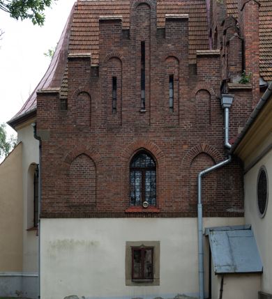 Zdjęcie nr 9: Kościół orientowany, murowany z cegły i kamienia, jednonawowy z trójprzęsłowym prezbiterium zamkniętym wielobocznie, sklepionym krzyżowo-żebrowo. Od północy umieszczona prostokątna, piętrowa zakrystia sklepiona kolebkowo (pięterko nad zakrystią dodane w 1885), dostępna kamiennym portalem o wykroju prostokątnym od strony wschodniej. Ściana północna zakrystii zakończona schodkowo z dekoracją blendową. Również od północy, na szerokości nawy do kościoła przylega prostokątna kaplica nakryta dachem czterospadowym zwieńczonym czworoboczną wieżyczką dostępna od zachodu przez prostokątną kruchtę z portalem o wykroju prostokątnym ujętym dwulalkowymi, kamiennymi balaskami. Kruchta zwieńczona trójkątnym przyczółkiem, na którym kamienny krzyż. Trójprzęsłowa nawa wyższa i szersza od prezbiterium i przesunięta w stosunku do jego osi ku stronie północnej, nakryta stropem. Północny mur nawy w części zachodniej poszerzony do pewnej wysokości dla pomieszczenia w jego grubości schodów prowadzących na chór muzyczny. Okna prostokątne zamknięte łukiem półkolistym. Zachodni i wschodni szczyt nawy zamknięty schodkowo. Od strony wschodniej trzy ostrołukowe blendy, w środkowej, wyżej od bocznych umieszczona tarcza herbowa z wizerunkiem św. Stanisława oraz Orła Białego. Od południa do nawy przylega prostokątna kruchta z kamiennym, ostrołukowym portalem nakryta dachem pulpitowym. Od strony zachodniej do bryły kościoła dostawiona prostokątna, współczesna kruchta wraz z chórem muzycznym (dobudowana w 1966) dostępna portalem o wykroju prostokątnym, nakryta dwuspadowym dachem. W ścianach bocznych wąskie, smukłe okna w kształcie stojącego prostokąta. Ponad kruchtą ażurowa dzwonnica na rzucie trójkąta zwieńczona krzyżem. Wieżyczka na sygnaturkę na rzucie ośmioboku zwieńczona barokowym hełmem z glorietą i krzyżem. Od zewnątrz kościół częściowo tynkowany, nawa i prezbiterium opięte szkarpami. Dachy kryte dachówką oraz blachą (część wschodnia prezbiterium).
