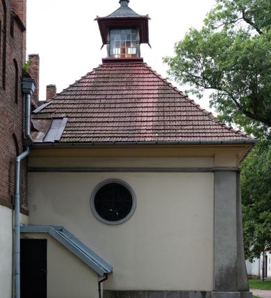Zdjęcie nr 15: Kościół orientowany, murowany z cegły i kamienia, jednonawowy z trójprzęsłowym prezbiterium zamkniętym wielobocznie, sklepionym krzyżowo-żebrowo. Od północy umieszczona prostokątna, piętrowa zakrystia sklepiona kolebkowo (pięterko nad zakrystią dodane w 1885), dostępna kamiennym portalem o wykroju prostokątnym od strony wschodniej. Ściana północna zakrystii zakończona schodkowo z dekoracją blendową. Również od północy, na szerokości nawy do kościoła przylega prostokątna kaplica nakryta dachem czterospadowym zwieńczonym czworoboczną wieżyczką dostępna od zachodu przez prostokątną kruchtę z portalem o wykroju prostokątnym ujętym dwulalkowymi, kamiennymi balaskami. Kruchta zwieńczona trójkątnym przyczółkiem, na którym kamienny krzyż. Trójprzęsłowa nawa wyższa i szersza od prezbiterium i przesunięta w stosunku do jego osi ku stronie północnej, nakryta stropem. Północny mur nawy w części zachodniej poszerzony do pewnej wysokości dla pomieszczenia w jego grubości schodów prowadzących na chór muzyczny. Okna prostokątne zamknięte łukiem półkolistym. Zachodni i wschodni szczyt nawy zamknięty schodkowo. Od strony wschodniej trzy ostrołukowe blendy, w środkowej, wyżej od bocznych umieszczona tarcza herbowa z wizerunkiem św. Stanisława oraz Orła Białego. Od południa do nawy przylega prostokątna kruchta z kamiennym, ostrołukowym portalem nakryta dachem pulpitowym. Od strony zachodniej do bryły kościoła dostawiona prostokątna, współczesna kruchta wraz z chórem muzycznym (dobudowana w 1966) dostępna portalem o wykroju prostokątnym, nakryta dwuspadowym dachem. W ścianach bocznych wąskie, smukłe okna w kształcie stojącego prostokąta. Ponad kruchtą ażurowa dzwonnica na rzucie trójkąta zwieńczona krzyżem. Wieżyczka na sygnaturkę na rzucie ośmioboku zwieńczona barokowym hełmem z glorietą i krzyżem. Od zewnątrz kościół częściowo tynkowany, nawa i prezbiterium opięte szkarpami. Dachy kryte dachówką oraz blachą (część wschodnia prezbiterium).