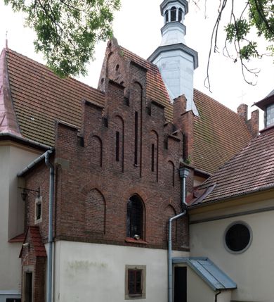 Zdjęcie nr 13: Kościół orientowany, murowany z cegły i kamienia, jednonawowy z trójprzęsłowym prezbiterium zamkniętym wielobocznie, sklepionym krzyżowo-żebrowo. Od północy umieszczona prostokątna, piętrowa zakrystia sklepiona kolebkowo (pięterko nad zakrystią dodane w 1885), dostępna kamiennym portalem o wykroju prostokątnym od strony wschodniej. Ściana północna zakrystii zakończona schodkowo z dekoracją blendową. Również od północy, na szerokości nawy do kościoła przylega prostokątna kaplica nakryta dachem czterospadowym zwieńczonym czworoboczną wieżyczką dostępna od zachodu przez prostokątną kruchtę z portalem o wykroju prostokątnym ujętym dwulalkowymi, kamiennymi balaskami. Kruchta zwieńczona trójkątnym przyczółkiem, na którym kamienny krzyż. Trójprzęsłowa nawa wyższa i szersza od prezbiterium i przesunięta w stosunku do jego osi ku stronie północnej, nakryta stropem. Północny mur nawy w części zachodniej poszerzony do pewnej wysokości dla pomieszczenia w jego grubości schodów prowadzących na chór muzyczny. Okna prostokątne zamknięte łukiem półkolistym. Zachodni i wschodni szczyt nawy zamknięty schodkowo. Od strony wschodniej trzy ostrołukowe blendy, w środkowej, wyżej od bocznych umieszczona tarcza herbowa z wizerunkiem św. Stanisława oraz Orła Białego. Od południa do nawy przylega prostokątna kruchta z kamiennym, ostrołukowym portalem nakryta dachem pulpitowym. Od strony zachodniej do bryły kościoła dostawiona prostokątna, współczesna kruchta wraz z chórem muzycznym (dobudowana w 1966) dostępna portalem o wykroju prostokątnym, nakryta dwuspadowym dachem. W ścianach bocznych wąskie, smukłe okna w kształcie stojącego prostokąta. Ponad kruchtą ażurowa dzwonnica na rzucie trójkąta zwieńczona krzyżem. Wieżyczka na sygnaturkę na rzucie ośmioboku zwieńczona barokowym hełmem z glorietą i krzyżem. Od zewnątrz kościół częściowo tynkowany, nawa i prezbiterium opięte szkarpami. Dachy kryte dachówką oraz blachą (część wschodnia prezbiterium).