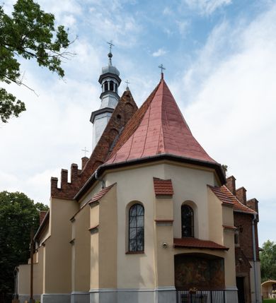 Zdjęcie nr 6: Kościół orientowany, murowany z cegły i kamienia, jednonawowy z trójprzęsłowym prezbiterium zamkniętym wielobocznie, sklepionym krzyżowo-żebrowo. Od północy umieszczona prostokątna, piętrowa zakrystia sklepiona kolebkowo (pięterko nad zakrystią dodane w 1885), dostępna kamiennym portalem o wykroju prostokątnym od strony wschodniej. Ściana północna zakrystii zakończona schodkowo z dekoracją blendową. Również od północy, na szerokości nawy do kościoła przylega prostokątna kaplica nakryta dachem czterospadowym zwieńczonym czworoboczną wieżyczką dostępna od zachodu przez prostokątną kruchtę z portalem o wykroju prostokątnym ujętym dwulalkowymi, kamiennymi balaskami. Kruchta zwieńczona trójkątnym przyczółkiem, na którym kamienny krzyż. Trójprzęsłowa nawa wyższa i szersza od prezbiterium i przesunięta w stosunku do jego osi ku stronie północnej, nakryta stropem. Północny mur nawy w części zachodniej poszerzony do pewnej wysokości dla pomieszczenia w jego grubości schodów prowadzących na chór muzyczny. Okna prostokątne zamknięte łukiem półkolistym. Zachodni i wschodni szczyt nawy zamknięty schodkowo. Od strony wschodniej trzy ostrołukowe blendy, w środkowej, wyżej od bocznych umieszczona tarcza herbowa z wizerunkiem św. Stanisława oraz Orła Białego. Od południa do nawy przylega prostokątna kruchta z kamiennym, ostrołukowym portalem nakryta dachem pulpitowym. Od strony zachodniej do bryły kościoła dostawiona prostokątna, współczesna kruchta wraz z chórem muzycznym (dobudowana w 1966) dostępna portalem o wykroju prostokątnym, nakryta dwuspadowym dachem. W ścianach bocznych wąskie, smukłe okna w kształcie stojącego prostokąta. Ponad kruchtą ażurowa dzwonnica na rzucie trójkąta zwieńczona krzyżem. Wieżyczka na sygnaturkę na rzucie ośmioboku zwieńczona barokowym hełmem z glorietą i krzyżem. Od zewnątrz kościół częściowo tynkowany, nawa i prezbiterium opięte szkarpami. Dachy kryte dachówką oraz blachą (część wschodnia prezbiterium).