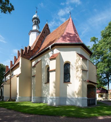 Zdjęcie nr 29: Kościół orientowany, murowany z cegły i kamienia, jednonawowy z trójprzęsłowym prezbiterium zamkniętym wielobocznie, sklepionym krzyżowo-żebrowo. Od północy umieszczona prostokątna, piętrowa zakrystia sklepiona kolebkowo (pięterko nad zakrystią dodane w 1885), dostępna kamiennym portalem o wykroju prostokątnym od strony wschodniej. Ściana północna zakrystii zakończona schodkowo z dekoracją blendową. Również od północy, na szerokości nawy do kościoła przylega prostokątna kaplica nakryta dachem czterospadowym zwieńczonym czworoboczną wieżyczką dostępna od zachodu przez prostokątną kruchtę z portalem o wykroju prostokątnym ujętym dwulalkowymi, kamiennymi balaskami. Kruchta zwieńczona trójkątnym przyczółkiem, na którym kamienny krzyż. Trójprzęsłowa nawa wyższa i szersza od prezbiterium i przesunięta w stosunku do jego osi ku stronie północnej, nakryta stropem. Północny mur nawy w części zachodniej poszerzony do pewnej wysokości dla pomieszczenia w jego grubości schodów prowadzących na chór muzyczny. Okna prostokątne zamknięte łukiem półkolistym. Zachodni i wschodni szczyt nawy zamknięty schodkowo. Od strony wschodniej trzy ostrołukowe blendy, w środkowej, wyżej od bocznych umieszczona tarcza herbowa z wizerunkiem św. Stanisława oraz Orła Białego. Od południa do nawy przylega prostokątna kruchta z kamiennym, ostrołukowym portalem nakryta dachem pulpitowym. Od strony zachodniej do bryły kościoła dostawiona prostokątna, współczesna kruchta wraz z chórem muzycznym (dobudowana w 1966) dostępna portalem o wykroju prostokątnym, nakryta dwuspadowym dachem. W ścianach bocznych wąskie, smukłe okna w kształcie stojącego prostokąta. Ponad kruchtą ażurowa dzwonnica na rzucie trójkąta zwieńczona krzyżem. Wieżyczka na sygnaturkę na rzucie ośmioboku zwieńczona barokowym hełmem z glorietą i krzyżem. Od zewnątrz kościół częściowo tynkowany, nawa i prezbiterium opięte szkarpami. Dachy kryte dachówką oraz blachą (część wschodnia prezbiterium).