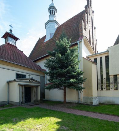 Zdjęcie nr 42: Kościół orientowany, murowany z cegły i kamienia, jednonawowy z trójprzęsłowym prezbiterium zamkniętym wielobocznie, sklepionym krzyżowo-żebrowo. Od północy umieszczona prostokątna, piętrowa zakrystia sklepiona kolebkowo (pięterko nad zakrystią dodane w 1885), dostępna kamiennym portalem o wykroju prostokątnym od strony wschodniej. Ściana północna zakrystii zakończona schodkowo z dekoracją blendową. Również od północy, na szerokości nawy do kościoła przylega prostokątna kaplica nakryta dachem czterospadowym zwieńczonym czworoboczną wieżyczką dostępna od zachodu przez prostokątną kruchtę z portalem o wykroju prostokątnym ujętym dwulalkowymi, kamiennymi balaskami. Kruchta zwieńczona trójkątnym przyczółkiem, na którym kamienny krzyż. Trójprzęsłowa nawa wyższa i szersza od prezbiterium i przesunięta w stosunku do jego osi ku stronie północnej, nakryta stropem. Północny mur nawy w części zachodniej poszerzony do pewnej wysokości dla pomieszczenia w jego grubości schodów prowadzących na chór muzyczny. Okna prostokątne zamknięte łukiem półkolistym. Zachodni i wschodni szczyt nawy zamknięty schodkowo. Od strony wschodniej trzy ostrołukowe blendy, w środkowej, wyżej od bocznych umieszczona tarcza herbowa z wizerunkiem św. Stanisława oraz Orła Białego. Od południa do nawy przylega prostokątna kruchta z kamiennym, ostrołukowym portalem nakryta dachem pulpitowym. Od strony zachodniej do bryły kościoła dostawiona prostokątna, współczesna kruchta wraz z chórem muzycznym (dobudowana w 1966) dostępna portalem o wykroju prostokątnym, nakryta dwuspadowym dachem. W ścianach bocznych wąskie, smukłe okna w kształcie stojącego prostokąta. Ponad kruchtą ażurowa dzwonnica na rzucie trójkąta zwieńczona krzyżem. Wieżyczka na sygnaturkę na rzucie ośmioboku zwieńczona barokowym hełmem z glorietą i krzyżem. Od zewnątrz kościół częściowo tynkowany, nawa i prezbiterium opięte szkarpami. Dachy kryte dachówką oraz blachą (część wschodnia prezbiterium).