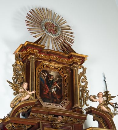 Zdjęcie nr 1: Ołtarz architektoniczny, dwukondygnacyjny, jednoosiowy ze zwieńczeniem. Mensa prostopadłościenna, antepedium w kształcie leżącego prostokąta, flankowane dwoma kanelowanymi pilastrami. W polu płycina w kształcie leżącego prostokąta wypełniona symetryczną dekoracją z akantu na czerwonym tle z sercem przebitym mieczem pośrodku. Cokół nastawy ustawiony na jednym stopniu, pośrodku zdobiony płyciną w kształcie leżącego prostokąta o zaokrąglonych krótszych bokach, cokoły pod kolumnami dekorowane mniejszymi płycinami wypełnionymi dekoracją roślinną. Pierwsza kondygnacja ujęta parą kolumn dźwigających przerwane belkowanie z przyczółkami, po bokach dodatkowo flankowana uszami wykończonymi ornamentem małżowinowo-chrząstkowym. W polu głównym obraz Najświętsze Serce Jezusa. Po bokach nastawy dwie rzeźby: po prawej św. Kazimierz Królewicz, a po lewej św. Alojzy Gonzaga. Na przyczółkach usadzone dwie rzeźby aniołów z rozłożonymi szeroko rękami. Kolumny ustawione na tle prostokątnych płycin, z bazami, trzony gładkie, kapitele kompozytowe. Druga kondygnacja flankowana parą kolumn podtrzymujących wyłamane belkowanie. W polu, w ramie o kształcie stojącego prostokąta o ściętych narożach obraz św. Michała Archanioła. W zwieńczeniu promienista gloria z monogramem Chrystusa na czerwonym tle, obwiedzionym wieńcem z obłoków. Zwieńczenie ujęte po bokach uszami. Struktura malowana w kolorze naturalnego drewna, ornamentyka złocona, detale srebrzone i czerwone.
