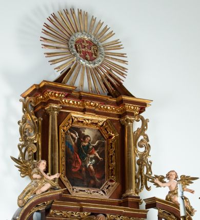 Zdjęcie nr 2: Ołtarz architektoniczny, dwukondygnacyjny, jednoosiowy ze zwieńczeniem. Mensa prostopadłościenna, antepedium w kształcie leżącego prostokąta, flankowane dwoma kanelowanymi pilastrami. W polu płycina w kształcie leżącego prostokąta wypełniona symetryczną dekoracją z akantu na czerwonym tle z sercem przebitym mieczem pośrodku. Cokół nastawy ustawiony na jednym stopniu, pośrodku zdobiony płyciną w kształcie leżącego prostokąta o zaokrąglonych krótszych bokach, cokoły pod kolumnami dekorowane mniejszymi płycinami wypełnionymi dekoracją roślinną. Pierwsza kondygnacja ujęta parą kolumn dźwigających przerwane belkowanie z przyczółkami, po bokach dodatkowo flankowana uszami wykończonymi ornamentem małżowinowo-chrząstkowym. W polu głównym obraz Najświętsze Serce Jezusa. Po bokach nastawy dwie rzeźby: po prawej św. Kazimierz Królewicz, a po lewej św. Alojzy Gonzaga. Na przyczółkach usadzone dwie rzeźby aniołów z rozłożonymi szeroko rękami. Kolumny ustawione na tle prostokątnych płycin, z bazami, trzony gładkie, kapitele kompozytowe. Druga kondygnacja flankowana parą kolumn podtrzymujących wyłamane belkowanie. W polu, w ramie o kształcie stojącego prostokąta o ściętych narożach obraz św. Michała Archanioła. W zwieńczeniu promienista gloria z monogramem Chrystusa na czerwonym tle, obwiedzionym wieńcem z obłoków. Zwieńczenie ujęte po bokach uszami. Struktura malowana w kolorze naturalnego drewna, ornamentyka złocona, detale srebrzone i czerwone.
