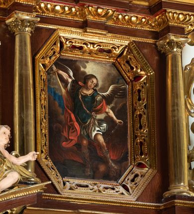 Zdjęcie nr 19: Ołtarz architektoniczny, dwukondygnacyjny, jednoosiowy ze zwieńczeniem. Mensa prostopadłościenna, antepedium w kształcie leżącego prostokąta, flankowane dwoma kanelowanymi pilastrami. W polu płycina w kształcie leżącego prostokąta wypełniona symetryczną dekoracją z akantu na czerwonym tle z sercem przebitym mieczem pośrodku. Cokół nastawy ustawiony na jednym stopniu, pośrodku zdobiony płyciną w kształcie leżącego prostokąta o zaokrąglonych krótszych bokach, cokoły pod kolumnami dekorowane mniejszymi płycinami wypełnionymi dekoracją roślinną. Pierwsza kondygnacja ujęta parą kolumn dźwigających przerwane belkowanie z przyczółkami, po bokach dodatkowo flankowana uszami wykończonymi ornamentem małżowinowo-chrząstkowym. W polu głównym obraz Najświętsze Serce Jezusa. Po bokach nastawy dwie rzeźby: po prawej św. Kazimierz Królewicz, a po lewej św. Alojzy Gonzaga. Na przyczółkach usadzone dwie rzeźby aniołów z rozłożonymi szeroko rękami. Kolumny ustawione na tle prostokątnych płycin, z bazami, trzony gładkie, kapitele kompozytowe. Druga kondygnacja flankowana parą kolumn podtrzymujących wyłamane belkowanie. W polu, w ramie o kształcie stojącego prostokąta o ściętych narożach obraz św. Michała Archanioła. W zwieńczeniu promienista gloria z monogramem Chrystusa na czerwonym tle, obwiedzionym wieńcem z obłoków. Zwieńczenie ujęte po bokach uszami. Struktura malowana w kolorze naturalnego drewna, ornamentyka złocona, detale srebrzone i czerwone.
