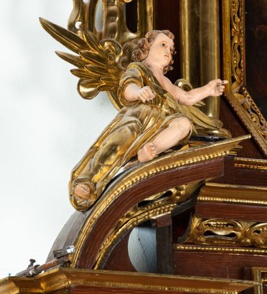 Zdjęcie nr 9: Ołtarz architektoniczny, dwukondygnacyjny, jednoosiowy ze zwieńczeniem. Mensa prostopadłościenna, antepedium w kształcie leżącego prostokąta, flankowane dwoma kanelowanymi pilastrami. W polu płycina w kształcie leżącego prostokąta wypełniona symetryczną dekoracją z akantu na czerwonym tle z sercem przebitym mieczem pośrodku. Cokół nastawy ustawiony na jednym stopniu, pośrodku zdobiony płyciną w kształcie leżącego prostokąta o zaokrąglonych krótszych bokach, cokoły pod kolumnami dekorowane mniejszymi płycinami wypełnionymi dekoracją roślinną. Pierwsza kondygnacja ujęta parą kolumn dźwigających przerwane belkowanie z przyczółkami, po bokach dodatkowo flankowana uszami wykończonymi ornamentem małżowinowo-chrząstkowym. W polu głównym obraz Najświętsze Serce Jezusa. Po bokach nastawy dwie rzeźby: po prawej św. Kazimierz Królewicz, a po lewej św. Alojzy Gonzaga. Na przyczółkach usadzone dwie rzeźby aniołów z rozłożonymi szeroko rękami. Kolumny ustawione na tle prostokątnych płycin, z bazami, trzony gładkie, kapitele kompozytowe. Druga kondygnacja flankowana parą kolumn podtrzymujących wyłamane belkowanie. W polu, w ramie o kształcie stojącego prostokąta o ściętych narożach obraz św. Michała Archanioła. W zwieńczeniu promienista gloria z monogramem Chrystusa na czerwonym tle, obwiedzionym wieńcem z obłoków. Zwieńczenie ujęte po bokach uszami. Struktura malowana w kolorze naturalnego drewna, ornamentyka złocona, detale srebrzone i czerwone.
