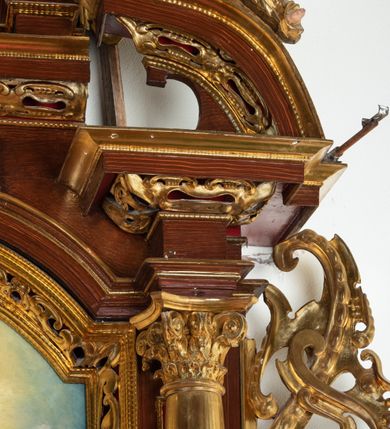 Zdjęcie nr 21: Ołtarz architektoniczny, dwukondygnacyjny, jednoosiowy ze zwieńczeniem. Mensa prostopadłościenna, antepedium w kształcie leżącego prostokąta, flankowane dwoma kanelowanymi pilastrami. W polu płycina w kształcie leżącego prostokąta wypełniona symetryczną dekoracją z akantu na czerwonym tle z sercem przebitym mieczem pośrodku. Cokół nastawy ustawiony na jednym stopniu, pośrodku zdobiony płyciną w kształcie leżącego prostokąta o zaokrąglonych krótszych bokach, cokoły pod kolumnami dekorowane mniejszymi płycinami wypełnionymi dekoracją roślinną. Pierwsza kondygnacja ujęta parą kolumn dźwigających przerwane belkowanie z przyczółkami, po bokach dodatkowo flankowana uszami wykończonymi ornamentem małżowinowo-chrząstkowym. W polu głównym obraz Najświętsze Serce Jezusa. Po bokach nastawy dwie rzeźby: po prawej św. Kazimierz Królewicz, a po lewej św. Alojzy Gonzaga. Na przyczółkach usadzone dwie rzeźby aniołów z rozłożonymi szeroko rękami. Kolumny ustawione na tle prostokątnych płycin, z bazami, trzony gładkie, kapitele kompozytowe. Druga kondygnacja flankowana parą kolumn podtrzymujących wyłamane belkowanie. W polu, w ramie o kształcie stojącego prostokąta o ściętych narożach obraz św. Michała Archanioła. W zwieńczeniu promienista gloria z monogramem Chrystusa na czerwonym tle, obwiedzionym wieńcem z obłoków. Zwieńczenie ujęte po bokach uszami. Struktura malowana w kolorze naturalnego drewna, ornamentyka złocona, detale srebrzone i czerwone.
