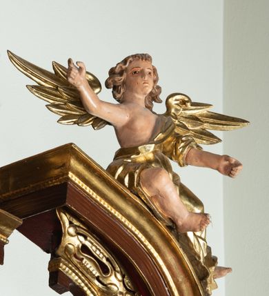 Zdjęcie nr 14: Ołtarz architektoniczny, dwukondygnacyjny, jednoosiowy ze zwieńczeniem. Mensa prostopadłościenna, antepedium w kształcie leżącego prostokąta, flankowane dwoma kanelowanymi pilastrami. W polu płycina w kształcie leżącego prostokąta wypełniona symetryczną dekoracją z akantu na czerwonym tle z sercem przebitym mieczem pośrodku. Cokół nastawy ustawiony na jednym stopniu, pośrodku zdobiony płyciną w kształcie leżącego prostokąta o zaokrąglonych krótszych bokach, cokoły pod kolumnami dekorowane mniejszymi płycinami wypełnionymi dekoracją roślinną. Pierwsza kondygnacja ujęta parą kolumn dźwigających przerwane belkowanie z przyczółkami, po bokach dodatkowo flankowana uszami wykończonymi ornamentem małżowinowo-chrząstkowym. W polu głównym obraz Najświętsze Serce Jezusa. Po bokach nastawy dwie rzeźby: po prawej św. Kazimierz Królewicz, a po lewej św. Alojzy Gonzaga. Na przyczółkach usadzone dwie rzeźby aniołów z rozłożonymi szeroko rękami. Kolumny ustawione na tle prostokątnych płycin, z bazami, trzony gładkie, kapitele kompozytowe. Druga kondygnacja flankowana parą kolumn podtrzymujących wyłamane belkowanie. W polu, w ramie o kształcie stojącego prostokąta o ściętych narożach obraz św. Michała Archanioła. W zwieńczeniu promienista gloria z monogramem Chrystusa na czerwonym tle, obwiedzionym wieńcem z obłoków. Zwieńczenie ujęte po bokach uszami. Struktura malowana w kolorze naturalnego drewna, ornamentyka złocona, detale srebrzone i czerwone.
