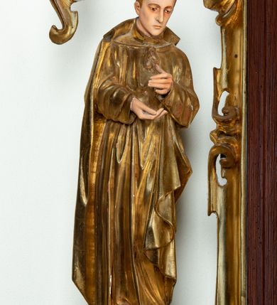 Zdjęcie nr 3: Ołtarz architektoniczny, dwukondygnacyjny, jednoosiowy ze zwieńczeniem. Mensa prostopadłościenna, antepedium w kształcie leżącego prostokąta, flankowane dwoma kanelowanymi pilastrami. W polu płycina w kształcie leżącego prostokąta wypełniona symetryczną dekoracją z akantu na czerwonym tle z sercem przebitym mieczem pośrodku. Cokół nastawy ustawiony na jednym stopniu, pośrodku zdobiony płyciną w kształcie leżącego prostokąta o zaokrąglonych krótszych bokach, cokoły pod kolumnami dekorowane mniejszymi płycinami wypełnionymi dekoracją roślinną. Pierwsza kondygnacja ujęta parą kolumn dźwigających przerwane belkowanie z przyczółkami, po bokach dodatkowo flankowana uszami wykończonymi ornamentem małżowinowo-chrząstkowym. W polu głównym obraz Najświętsze Serce Jezusa. Po bokach nastawy dwie rzeźby: po prawej św. Kazimierz Królewicz, a po lewej św. Alojzy Gonzaga. Na przyczółkach usadzone dwie rzeźby aniołów z rozłożonymi szeroko rękami. Kolumny ustawione na tle prostokątnych płycin, z bazami, trzony gładkie, kapitele kompozytowe. Druga kondygnacja flankowana parą kolumn podtrzymujących wyłamane belkowanie. W polu, w ramie o kształcie stojącego prostokąta o ściętych narożach obraz św. Michała Archanioła. W zwieńczeniu promienista gloria z monogramem Chrystusa na czerwonym tle, obwiedzionym wieńcem z obłoków. Zwieńczenie ujęte po bokach uszami. Struktura malowana w kolorze naturalnego drewna, ornamentyka złocona, detale srebrzone i czerwone.
