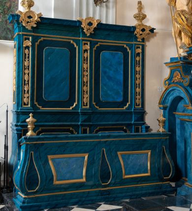 Zdjęcie nr 1: Dwie stalle o siedziskach obudowanych z przodu wybrzuszonymi ściankami z wazonami na pulpitach. Siedziska wybrzuszone z boku są ujęte falistymi poręczami, z plecami zdobionymi profilowanymi płycinami prostokątnymi o ściętych ćwierćkoliście narożach. Znajdujące się nad nimi wysokie zaplecki są ujęte pilastrami zdobionymi płycinami wypełnionymi wiciami liści i kwiatów z muszlami a z boku kampanuli, zwieńczone belkowaniem. W dwóch polach pomiędzy pilastrami zdwojone płyciny wyróżnione profilami w kształcie prostokątów o wyciętych ćwierćkoliście narożach.  Na belkowaniu trzy rokokowe kartusze i dwa płomieniste wazony. Polichromia imitująca jasno i ciemnoniebieską marmoryzację, ornamenty i profile złocone.  

Dwie stalle bez obudowy i wysokich zaplecków na falistych nogach, z których zewnętrzne poprzedzone lwimi łapami, z falistymi poręczami i prostymi oparciami zwieńczonymi gzymsem. Oparcie podzielone na trzy pola oddzielone żłobkowaniami i rautami nad nimi i wypełnione profilowanymi, kwadratowymi płycinami o ściętych ćwierćkoliście narożach.       