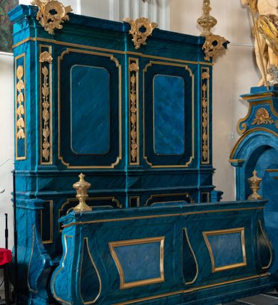 Zdjęcie nr 2: Dwie stalle o siedziskach obudowanych z przodu wybrzuszonymi ściankami z wazonami na pulpitach. Siedziska wybrzuszone z boku są ujęte falistymi poręczami, z plecami zdobionymi profilowanymi płycinami prostokątnymi o ściętych ćwierćkoliście narożach. Znajdujące się nad nimi wysokie zaplecki są ujęte pilastrami zdobionymi płycinami wypełnionymi wiciami liści i kwiatów z muszlami a z boku kampanuli, zwieńczone belkowaniem. W dwóch polach pomiędzy pilastrami zdwojone płyciny wyróżnione profilami w kształcie prostokątów o wyciętych ćwierćkoliście narożach.  Na belkowaniu trzy rokokowe kartusze i dwa płomieniste wazony. Polichromia imitująca jasno i ciemnoniebieską marmoryzację, ornamenty i profile złocone.  

Dwie stalle bez obudowy i wysokich zaplecków na falistych nogach, z których zewnętrzne poprzedzone lwimi łapami, z falistymi poręczami i prostymi oparciami zwieńczonymi gzymsem. Oparcie podzielone na trzy pola oddzielone żłobkowaniami i rautami nad nimi i wypełnione profilowanymi, kwadratowymi płycinami o ściętych ćwierćkoliście narożach.       