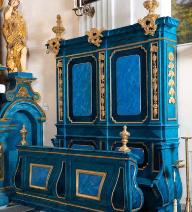 Zdjęcie nr 12: Dwie stalle o siedziskach obudowanych z przodu wybrzuszonymi ściankami z wazonami na pulpitach. Siedziska wybrzuszone z boku są ujęte falistymi poręczami, z plecami zdobionymi profilowanymi płycinami prostokątnymi o ściętych ćwierćkoliście narożach. Znajdujące się nad nimi wysokie zaplecki są ujęte pilastrami zdobionymi płycinami wypełnionymi wiciami liści i kwiatów z muszlami a z boku kampanuli, zwieńczone belkowaniem. W dwóch polach pomiędzy pilastrami zdwojone płyciny wyróżnione profilami w kształcie prostokątów o wyciętych ćwierćkoliście narożach.  Na belkowaniu trzy rokokowe kartusze i dwa płomieniste wazony. Polichromia imitująca jasno i ciemnoniebieską marmoryzację, ornamenty i profile złocone.  

Dwie stalle bez obudowy i wysokich zaplecków na falistych nogach, z których zewnętrzne poprzedzone lwimi łapami, z falistymi poręczami i prostymi oparciami zwieńczonymi gzymsem. Oparcie podzielone na trzy pola oddzielone żłobkowaniami i rautami nad nimi i wypełnione profilowanymi, kwadratowymi płycinami o ściętych ćwierćkoliście narożach.       