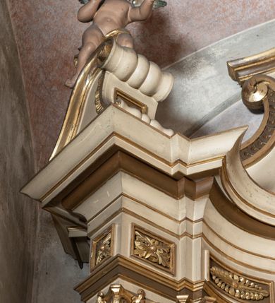 Zdjęcie nr 7: Przyścienna, jednokondygnacyjna, jednoosiowa nastawa ze zwieńczeniem uzyskała strukturę architektoniczną. Stipes ołtarzowy z drewnianą mensą z portatylem wykonano w kształcie sarkofagowym, ustawiając go na wysokim, fazowanym postumencie. Na nim znalazło się prostopadłościenne tabernakulum z obłym frontem udekorowanym prostokątnymi drzwiczkami zamkniętymi u góry nadwieszonym łukiem odcinkowy. Ich pole wypełnia płaskorzeźbione przedstawienie stojącego baranka apokaliptycznego. Całość wieńczy profilowany gzyms korrnujuacy utworzony z dwóch antetycznych wolut. Retabulum wsparto na dwuczęściowym, wysokim cokole. Kondygnację ujęto ustawionymi pod kątem opilastrowanymi, wklęsłymi filarami, przed którymi znalazła się para ustawionych pod kątem kolumn o kapitelach kompozytowych, usteweionyuch na postumentach o bokach dekorowanych prostokątnymi płycinami obramienionymi profilowanymi ramkami. Podpory dźwigają wyłamane imposty połączone ze sobą gzymsem. Na nim wsparto dwa falujące przyczółki, na których siedzi para putt. W polu kondygnacji umieszczono obraz Ukrzyżowania ujęty ramą w kształcie stojącego prostokąta zamkniętego u góry łukiem odcinkowym. Ponad nim na osi nastawę przepruto oculusem otwierającym się na okno witrażowe na wysokości przerwanego belkowania. Zwieńczenie ołtarza uzyskało kształt leżącego prostokąta o wklęsłych bokach utworzonych ze spływów wolutowych podtrzymujących profilowany gzyms koronujący powstały z dwóch antytetycznych wolut. W polu zwieńczenia umieszczono obraz św. Tytusa ujętego w fantazyjną ramę. Strukturę polichromowano na czarno. Głowice pilastrów i kapitele kolumn wyzłocono podobnie jak profile i obramowania. Rzeźby aniołków uzyskały naturalistyczną polichromię ze złoconymi przepaskami.   