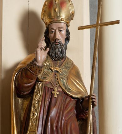 Zdjęcie nr 12: Przyścienna, jednokondygnacyjna, jednoosiowa nastawa ze zwieńczeniem uzyskała strukturę architektoniczną. Stipes ołtarzowy z drewnianą mensą z portatylem wykonano w kształcie sarkofagowym, ustawiając go na wysokim, fazowanym postumencie. Na nim znalazło się prostopadłościenne tabernakulum z obłym frontem udekorowanym prostokątnymi drzwiczkami zamkniętymi u góry nadwieszonym łukiem odcinkowy. Ich pole wypełnia płaskorzeźbione przedstawienie stojącego baranka apokaliptycznego. Całość wieńczy profilowany gzyms korrnujuacy utworzony z dwóch antetycznych wolut. Retabulum wsparto na dwuczęściowym, wysokim cokole. Kondygnację ujęto ustawionymi pod kątem opilastrowanymi, wklęsłymi filarami, przed którymi znalazła się para ustawionych pod kątem kolumn o kapitelach kompozytowych, usteweionyuch na postumentach o bokach dekorowanych prostokątnymi płycinami obramienionymi profilowanymi ramkami. Podpory dźwigają wyłamane imposty połączone ze sobą gzymsem. Na nim wsparto dwa falujące przyczółki, na których siedzi para putt. W polu kondygnacji umieszczono obraz Ukrzyżowania ujęty ramą w kształcie stojącego prostokąta zamkniętego u góry łukiem odcinkowym. Ponad nim na osi nastawę przepruto oculusem otwierającym się na okno witrażowe na wysokości przerwanego belkowania. Zwieńczenie ołtarza uzyskało kształt leżącego prostokąta o wklęsłych bokach utworzonych ze spływów wolutowych podtrzymujących profilowany gzyms koronujący powstały z dwóch antytetycznych wolut. W polu zwieńczenia umieszczono obraz św. Tytusa ujętego w fantazyjną ramę. Strukturę polichromowano na czarno. Głowice pilastrów i kapitele kolumn wyzłocono podobnie jak profile i obramowania. Rzeźby aniołków uzyskały naturalistyczną polichromię ze złoconymi przepaskami.   