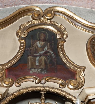 Zdjęcie nr 10: Przyścienna, jednokondygnacyjna, jednoosiowa nastawa ze zwieńczeniem uzyskała strukturę architektoniczną. Stipes ołtarzowy z drewnianą mensą z portatylem wykonano w kształcie sarkofagowym, ustawiając go na wysokim, fazowanym postumencie. Na nim znalazło się prostopadłościenne tabernakulum z obłym frontem udekorowanym prostokątnymi drzwiczkami zamkniętymi u góry nadwieszonym łukiem odcinkowy. Ich pole wypełnia płaskorzeźbione przedstawienie stojącego baranka apokaliptycznego. Całość wieńczy profilowany gzyms korrnujuacy utworzony z dwóch antetycznych wolut. Retabulum wsparto na dwuczęściowym, wysokim cokole. Kondygnację ujęto ustawionymi pod kątem opilastrowanymi, wklęsłymi filarami, przed którymi znalazła się para ustawionych pod kątem kolumn o kapitelach kompozytowych, usteweionyuch na postumentach o bokach dekorowanych prostokątnymi płycinami obramienionymi profilowanymi ramkami. Podpory dźwigają wyłamane imposty połączone ze sobą gzymsem. Na nim wsparto dwa falujące przyczółki, na których siedzi para putt. W polu kondygnacji umieszczono obraz Ukrzyżowania ujęty ramą w kształcie stojącego prostokąta zamkniętego u góry łukiem odcinkowym. Ponad nim na osi nastawę przepruto oculusem otwierającym się na okno witrażowe na wysokości przerwanego belkowania. Zwieńczenie ołtarza uzyskało kształt leżącego prostokąta o wklęsłych bokach utworzonych ze spływów wolutowych podtrzymujących profilowany gzyms koronujący powstały z dwóch antytetycznych wolut. W polu zwieńczenia umieszczono obraz św. Tytusa ujętego w fantazyjną ramę. Strukturę polichromowano na czarno. Głowice pilastrów i kapitele kolumn wyzłocono podobnie jak profile i obramowania. Rzeźby aniołków uzyskały naturalistyczną polichromię ze złoconymi przepaskami.   