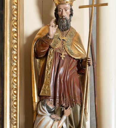 Zdjęcie nr 14: Przyścienna, jednokondygnacyjna, jednoosiowa nastawa ze zwieńczeniem uzyskała strukturę architektoniczną. Stipes ołtarzowy z drewnianą mensą z portatylem wykonano w kształcie sarkofagowym, ustawiając go na wysokim, fazowanym postumencie. Na nim znalazło się prostopadłościenne tabernakulum z obłym frontem udekorowanym prostokątnymi drzwiczkami zamkniętymi u góry nadwieszonym łukiem odcinkowy. Ich pole wypełnia płaskorzeźbione przedstawienie stojącego baranka apokaliptycznego. Całość wieńczy profilowany gzyms korrnujuacy utworzony z dwóch antetycznych wolut. Retabulum wsparto na dwuczęściowym, wysokim cokole. Kondygnację ujęto ustawionymi pod kątem opilastrowanymi, wklęsłymi filarami, przed którymi znalazła się para ustawionych pod kątem kolumn o kapitelach kompozytowych, usteweionyuch na postumentach o bokach dekorowanych prostokątnymi płycinami obramienionymi profilowanymi ramkami. Podpory dźwigają wyłamane imposty połączone ze sobą gzymsem. Na nim wsparto dwa falujące przyczółki, na których siedzi para putt. W polu kondygnacji umieszczono obraz Ukrzyżowania ujęty ramą w kształcie stojącego prostokąta zamkniętego u góry łukiem odcinkowym. Ponad nim na osi nastawę przepruto oculusem otwierającym się na okno witrażowe na wysokości przerwanego belkowania. Zwieńczenie ołtarza uzyskało kształt leżącego prostokąta o wklęsłych bokach utworzonych ze spływów wolutowych podtrzymujących profilowany gzyms koronujący powstały z dwóch antytetycznych wolut. W polu zwieńczenia umieszczono obraz św. Tytusa ujętego w fantazyjną ramę. Strukturę polichromowano na czarno. Głowice pilastrów i kapitele kolumn wyzłocono podobnie jak profile i obramowania. Rzeźby aniołków uzyskały naturalistyczną polichromię ze złoconymi przepaskami.   