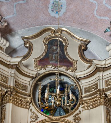 Zdjęcie nr 9: Przyścienna, jednokondygnacyjna, jednoosiowa nastawa ze zwieńczeniem uzyskała strukturę architektoniczną. Stipes ołtarzowy z drewnianą mensą z portatylem wykonano w kształcie sarkofagowym, ustawiając go na wysokim, fazowanym postumencie. Na nim znalazło się prostopadłościenne tabernakulum z obłym frontem udekorowanym prostokątnymi drzwiczkami zamkniętymi u góry nadwieszonym łukiem odcinkowy. Ich pole wypełnia płaskorzeźbione przedstawienie stojącego baranka apokaliptycznego. Całość wieńczy profilowany gzyms korrnujuacy utworzony z dwóch antetycznych wolut. Retabulum wsparto na dwuczęściowym, wysokim cokole. Kondygnację ujęto ustawionymi pod kątem opilastrowanymi, wklęsłymi filarami, przed którymi znalazła się para ustawionych pod kątem kolumn o kapitelach kompozytowych, usteweionyuch na postumentach o bokach dekorowanych prostokątnymi płycinami obramienionymi profilowanymi ramkami. Podpory dźwigają wyłamane imposty połączone ze sobą gzymsem. Na nim wsparto dwa falujące przyczółki, na których siedzi para putt. W polu kondygnacji umieszczono obraz Ukrzyżowania ujęty ramą w kształcie stojącego prostokąta zamkniętego u góry łukiem odcinkowym. Ponad nim na osi nastawę przepruto oculusem otwierającym się na okno witrażowe na wysokości przerwanego belkowania. Zwieńczenie ołtarza uzyskało kształt leżącego prostokąta o wklęsłych bokach utworzonych ze spływów wolutowych podtrzymujących profilowany gzyms koronujący powstały z dwóch antytetycznych wolut. W polu zwieńczenia umieszczono obraz św. Tytusa ujętego w fantazyjną ramę. Strukturę polichromowano na czarno. Głowice pilastrów i kapitele kolumn wyzłocono podobnie jak profile i obramowania. Rzeźby aniołków uzyskały naturalistyczną polichromię ze złoconymi przepaskami.   