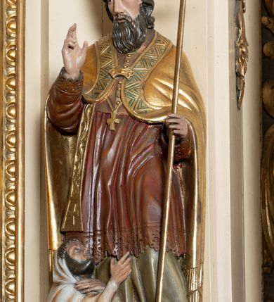 Zdjęcie nr 13: Przyścienna, jednokondygnacyjna, jednoosiowa nastawa ze zwieńczeniem uzyskała strukturę architektoniczną. Stipes ołtarzowy z drewnianą mensą z portatylem wykonano w kształcie sarkofagowym, ustawiając go na wysokim, fazowanym postumencie. Na nim znalazło się prostopadłościenne tabernakulum z obłym frontem udekorowanym prostokątnymi drzwiczkami zamkniętymi u góry nadwieszonym łukiem odcinkowy. Ich pole wypełnia płaskorzeźbione przedstawienie stojącego baranka apokaliptycznego. Całość wieńczy profilowany gzyms korrnujuacy utworzony z dwóch antetycznych wolut. Retabulum wsparto na dwuczęściowym, wysokim cokole. Kondygnację ujęto ustawionymi pod kątem opilastrowanymi, wklęsłymi filarami, przed którymi znalazła się para ustawionych pod kątem kolumn o kapitelach kompozytowych, usteweionyuch na postumentach o bokach dekorowanych prostokątnymi płycinami obramienionymi profilowanymi ramkami. Podpory dźwigają wyłamane imposty połączone ze sobą gzymsem. Na nim wsparto dwa falujące przyczółki, na których siedzi para putt. W polu kondygnacji umieszczono obraz Ukrzyżowania ujęty ramą w kształcie stojącego prostokąta zamkniętego u góry łukiem odcinkowym. Ponad nim na osi nastawę przepruto oculusem otwierającym się na okno witrażowe na wysokości przerwanego belkowania. Zwieńczenie ołtarza uzyskało kształt leżącego prostokąta o wklęsłych bokach utworzonych ze spływów wolutowych podtrzymujących profilowany gzyms koronujący powstały z dwóch antytetycznych wolut. W polu zwieńczenia umieszczono obraz św. Tytusa ujętego w fantazyjną ramę. Strukturę polichromowano na czarno. Głowice pilastrów i kapitele kolumn wyzłocono podobnie jak profile i obramowania. Rzeźby aniołków uzyskały naturalistyczną polichromię ze złoconymi przepaskami.   