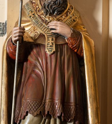 Zdjęcie nr 3: Przyścienna, jednokondygnacyjna, jednoosiowa nastawa ze zwieńczeniem uzyskała strukturę architektoniczną. Stipes ołtarzowy z drewnianą mensą z portatylem wykonano w kształcie sarkofagowym, ustawiając go na wysokim, fazowanym postumencie. Na nim znalazło się prostopadłościenne tabernakulum z obłym frontem udekorowanym prostokątnymi drzwiczkami zamkniętymi u góry nadwieszonym łukiem odcinkowy. Ich pole wypełnia płaskorzeźbione przedstawienie stojącego baranka apokaliptycznego. Całość wieńczy profilowany gzyms korrnujuacy utworzony z dwóch antetycznych wolut. Retabulum wsparto na dwuczęściowym, wysokim cokole. Kondygnację ujęto ustawionymi pod kątem opilastrowanymi, wklęsłymi filarami, przed którymi znalazła się para ustawionych pod kątem kolumn o kapitelach kompozytowych, usteweionyuch na postumentach o bokach dekorowanych prostokątnymi płycinami obramienionymi profilowanymi ramkami. Podpory dźwigają wyłamane imposty połączone ze sobą gzymsem. Na nim wsparto dwa falujące przyczółki, na których siedzi para putt. W polu kondygnacji umieszczono obraz Ukrzyżowania ujęty ramą w kształcie stojącego prostokąta zamkniętego u góry łukiem odcinkowym. Ponad nim na osi nastawę przepruto oculusem otwierającym się na okno witrażowe na wysokości przerwanego belkowania. Zwieńczenie ołtarza uzyskało kształt leżącego prostokąta o wklęsłych bokach utworzonych ze spływów wolutowych podtrzymujących profilowany gzyms koronujący powstały z dwóch antytetycznych wolut. W polu zwieńczenia umieszczono obraz św. Tytusa ujętego w fantazyjną ramę. Strukturę polichromowano na czarno. Głowice pilastrów i kapitele kolumn wyzłocono podobnie jak profile i obramowania. Rzeźby aniołków uzyskały naturalistyczną polichromię ze złoconymi przepaskami.   