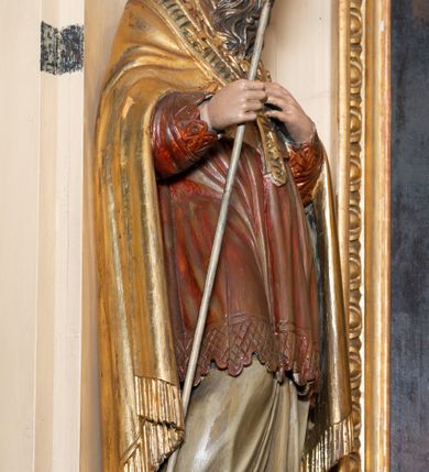 Zdjęcie nr 5: Przyścienna, jednokondygnacyjna, jednoosiowa nastawa ze zwieńczeniem uzyskała strukturę architektoniczną. Stipes ołtarzowy z drewnianą mensą z portatylem wykonano w kształcie sarkofagowym, ustawiając go na wysokim, fazowanym postumencie. Na nim znalazło się prostopadłościenne tabernakulum z obłym frontem udekorowanym prostokątnymi drzwiczkami zamkniętymi u góry nadwieszonym łukiem odcinkowy. Ich pole wypełnia płaskorzeźbione przedstawienie stojącego baranka apokaliptycznego. Całość wieńczy profilowany gzyms korrnujuacy utworzony z dwóch antetycznych wolut. Retabulum wsparto na dwuczęściowym, wysokim cokole. Kondygnację ujęto ustawionymi pod kątem opilastrowanymi, wklęsłymi filarami, przed którymi znalazła się para ustawionych pod kątem kolumn o kapitelach kompozytowych, usteweionyuch na postumentach o bokach dekorowanych prostokątnymi płycinami obramienionymi profilowanymi ramkami. Podpory dźwigają wyłamane imposty połączone ze sobą gzymsem. Na nim wsparto dwa falujące przyczółki, na których siedzi para putt. W polu kondygnacji umieszczono obraz Ukrzyżowania ujęty ramą w kształcie stojącego prostokąta zamkniętego u góry łukiem odcinkowym. Ponad nim na osi nastawę przepruto oculusem otwierającym się na okno witrażowe na wysokości przerwanego belkowania. Zwieńczenie ołtarza uzyskało kształt leżącego prostokąta o wklęsłych bokach utworzonych ze spływów wolutowych podtrzymujących profilowany gzyms koronujący powstały z dwóch antytetycznych wolut. W polu zwieńczenia umieszczono obraz św. Tytusa ujętego w fantazyjną ramę. Strukturę polichromowano na czarno. Głowice pilastrów i kapitele kolumn wyzłocono podobnie jak profile i obramowania. Rzeźby aniołków uzyskały naturalistyczną polichromię ze złoconymi przepaskami.   