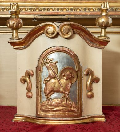 Zdjęcie nr 11: Przyścienna, jednokondygnacyjna, jednoosiowa nastawa ze zwieńczeniem uzyskała strukturę architektoniczną. Stipes ołtarzowy z drewnianą mensą z portatylem wykonano w kształcie sarkofagowym, ustawiając go na wysokim, fazowanym postumencie. Na nim znalazło się prostopadłościenne tabernakulum z obłym frontem udekorowanym prostokątnymi drzwiczkami zamkniętymi u góry nadwieszonym łukiem odcinkowy. Ich pole wypełnia płaskorzeźbione przedstawienie stojącego baranka apokaliptycznego. Całość wieńczy profilowany gzyms korrnujuacy utworzony z dwóch antetycznych wolut. Retabulum wsparto na dwuczęściowym, wysokim cokole. Kondygnację ujęto ustawionymi pod kątem opilastrowanymi, wklęsłymi filarami, przed którymi znalazła się para ustawionych pod kątem kolumn o kapitelach kompozytowych, usteweionyuch na postumentach o bokach dekorowanych prostokątnymi płycinami obramienionymi profilowanymi ramkami. Podpory dźwigają wyłamane imposty połączone ze sobą gzymsem. Na nim wsparto dwa falujące przyczółki, na których siedzi para putt. W polu kondygnacji umieszczono obraz Ukrzyżowania ujęty ramą w kształcie stojącego prostokąta zamkniętego u góry łukiem odcinkowym. Ponad nim na osi nastawę przepruto oculusem otwierającym się na okno witrażowe na wysokości przerwanego belkowania. Zwieńczenie ołtarza uzyskało kształt leżącego prostokąta o wklęsłych bokach utworzonych ze spływów wolutowych podtrzymujących profilowany gzyms koronujący powstały z dwóch antytetycznych wolut. W polu zwieńczenia umieszczono obraz św. Tytusa ujętego w fantazyjną ramę. Strukturę polichromowano na czarno. Głowice pilastrów i kapitele kolumn wyzłocono podobnie jak profile i obramowania. Rzeźby aniołków uzyskały naturalistyczną polichromię ze złoconymi przepaskami.   