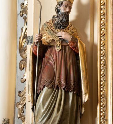 Zdjęcie nr 6: Przyścienna, jednokondygnacyjna, jednoosiowa nastawa ze zwieńczeniem uzyskała strukturę architektoniczną. Stipes ołtarzowy z drewnianą mensą z portatylem wykonano w kształcie sarkofagowym, ustawiając go na wysokim, fazowanym postumencie. Na nim znalazło się prostopadłościenne tabernakulum z obłym frontem udekorowanym prostokątnymi drzwiczkami zamkniętymi u góry nadwieszonym łukiem odcinkowy. Ich pole wypełnia płaskorzeźbione przedstawienie stojącego baranka apokaliptycznego. Całość wieńczy profilowany gzyms korrnujuacy utworzony z dwóch antetycznych wolut. Retabulum wsparto na dwuczęściowym, wysokim cokole. Kondygnację ujęto ustawionymi pod kątem opilastrowanymi, wklęsłymi filarami, przed którymi znalazła się para ustawionych pod kątem kolumn o kapitelach kompozytowych, usteweionyuch na postumentach o bokach dekorowanych prostokątnymi płycinami obramienionymi profilowanymi ramkami. Podpory dźwigają wyłamane imposty połączone ze sobą gzymsem. Na nim wsparto dwa falujące przyczółki, na których siedzi para putt. W polu kondygnacji umieszczono obraz Ukrzyżowania ujęty ramą w kształcie stojącego prostokąta zamkniętego u góry łukiem odcinkowym. Ponad nim na osi nastawę przepruto oculusem otwierającym się na okno witrażowe na wysokości przerwanego belkowania. Zwieńczenie ołtarza uzyskało kształt leżącego prostokąta o wklęsłych bokach utworzonych ze spływów wolutowych podtrzymujących profilowany gzyms koronujący powstały z dwóch antytetycznych wolut. W polu zwieńczenia umieszczono obraz św. Tytusa ujętego w fantazyjną ramę. Strukturę polichromowano na czarno. Głowice pilastrów i kapitele kolumn wyzłocono podobnie jak profile i obramowania. Rzeźby aniołków uzyskały naturalistyczną polichromię ze złoconymi przepaskami.   