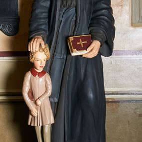 Zdjęcie nr 1: Rzeźba pełnoplastyczna ustawiona na trójstopniowym cokole przedstawiająca Jana Kantego. Święty stoi frontalnie, w kontrapoście, głowę przechyla na lewe ramię, patrzy przed siebie, w lewej, opuszczonej ręce trzyma zamkniętą księgę, prawą składa na głowie stojącego obok jego prawej nogi dziecka.  Ma pociągłą twarz, małe, ciemne oczy, prosty nos i wąskie usta, na czubku głowy szeroka łysina, po bokach falowane włosy zakrywające uszy. Jest ubrany w czarny habit przewiązany szerokim pasem i obszerny, czarny płaszcz; pod szyją widoczny biały kołnierzyk. Na nogach ma ciemnobrązowe buty. Dziecko sięga bioder Jana Kantego, stoi wyprostowane, głowę zwraca w lewo, ręce przyciska do ciała, prawą przytrzymuje czapkę (?). Ma pociągłą twarz, jasne oczy, wąskie brwi i nos praz pełne usta. Blond włosy formują loki wokół twarzy. Dziecko jest ubrane w różową sukienkę z bordowym kołnierzykiem i szare rajtuzy, na nogach ma brązowe buty. Postacie zostały ustawione na szarym, profilowanym, prostopadłościennym cokole, który stoi na kolejnym, dwustopniowym, marmoryzowanym i ze złoconymi krawędziami. Z przodu, na stopniu tabliczka z napisem „ŚW. JANIE KANTY / PROFESORZE / MÓDL SIĘ ZA NAMI”. 